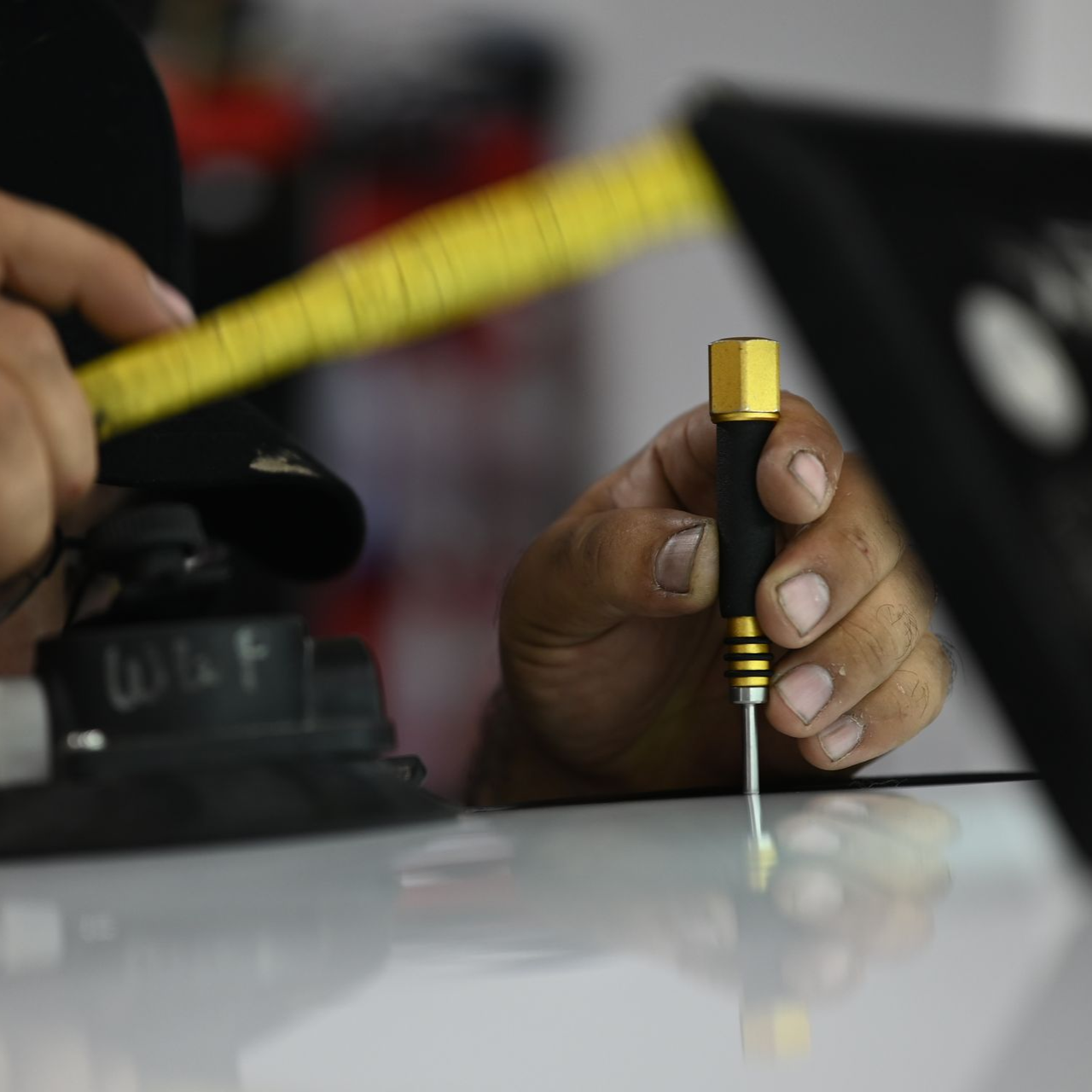 Man applying film to a car bumper with tools in a garage.