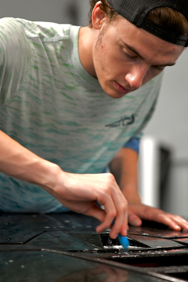 Person using a blue tool to work on a black surface in a workshop or studio