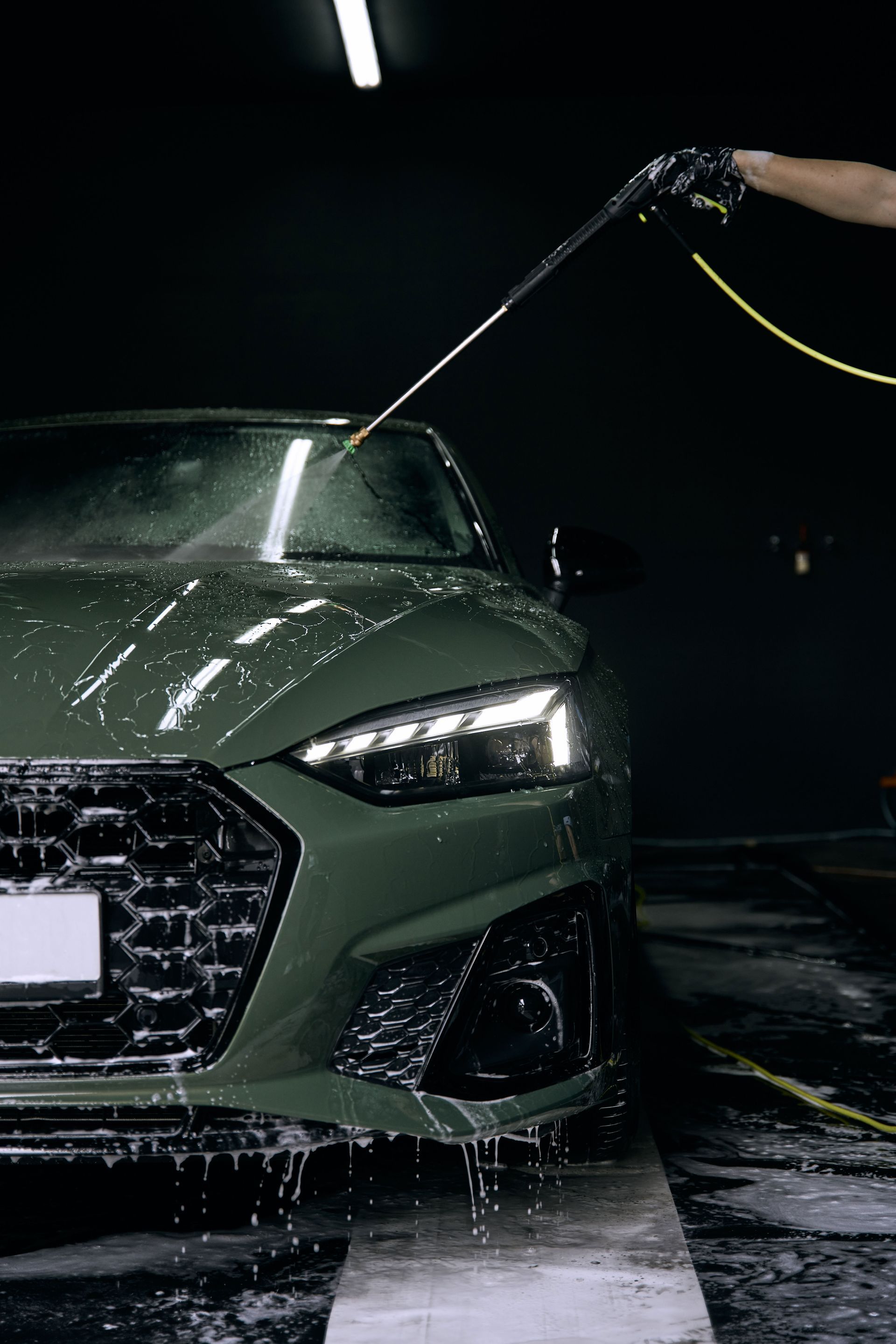 Green Audi being sprayed with water in a dark car wash, headlights on