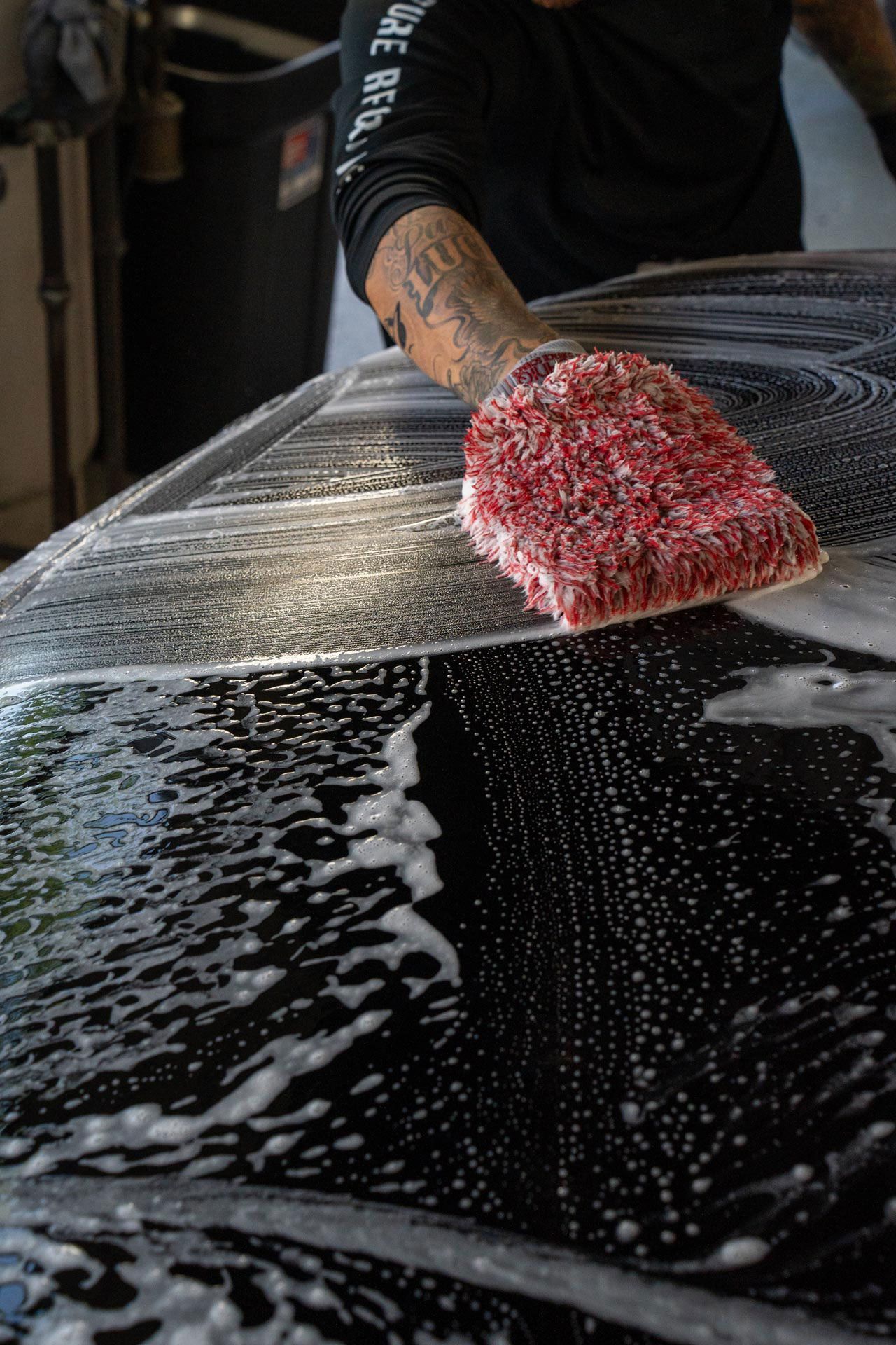 Person washing a black car with a red sponge and soap suds