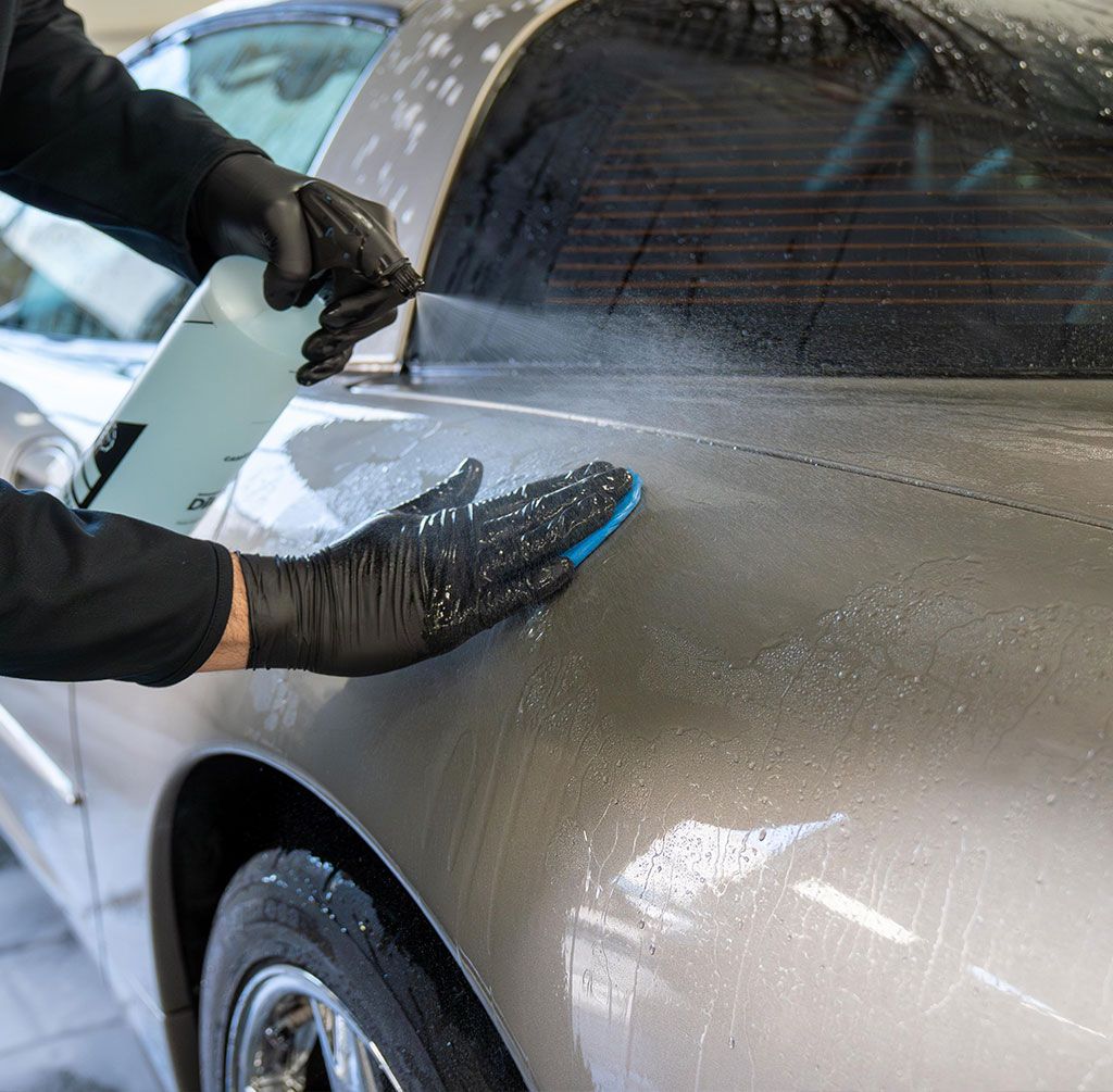 Gloved hands applying a protective film to a silver car window and door.