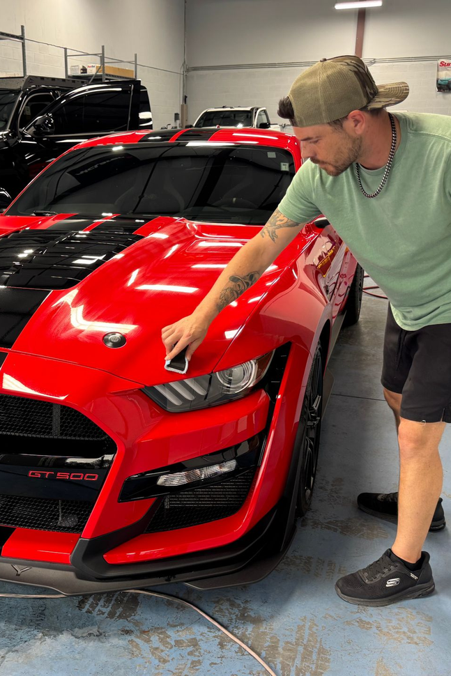Man pointing at the front of a red sports car in a garage
