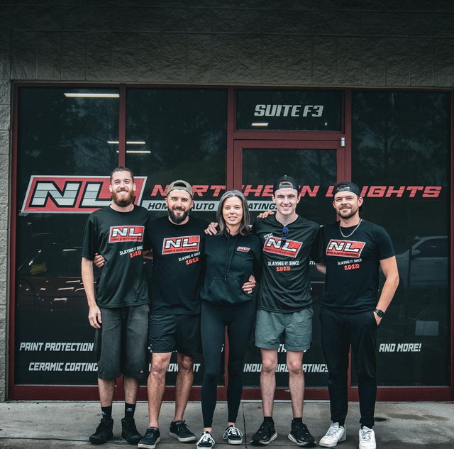 Five people in black North Team Nighte shirts standing outside a storefront with a red door