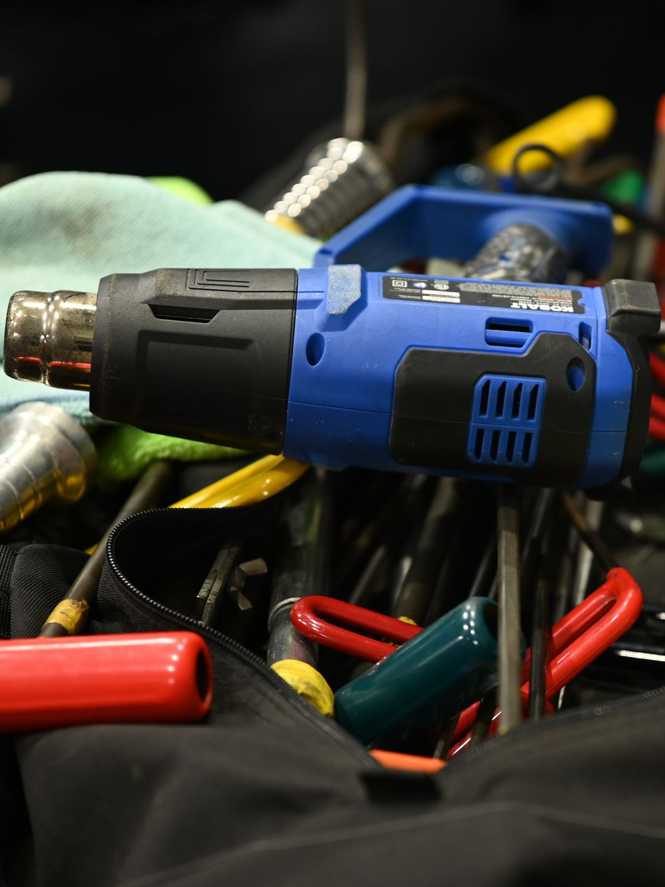 Person applying clear protective film to a black car's headlight, using tools and water spray.