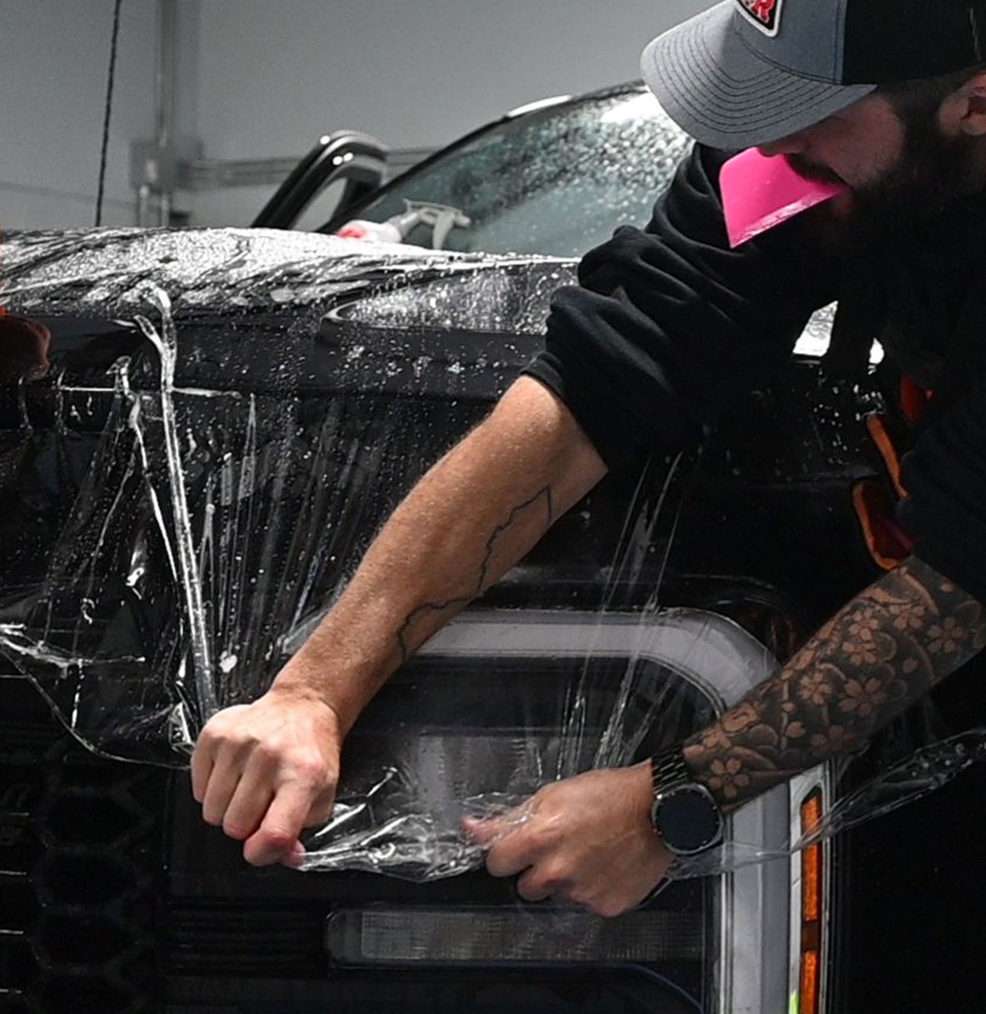 Person wrapping a black car in clear protective film in a garage