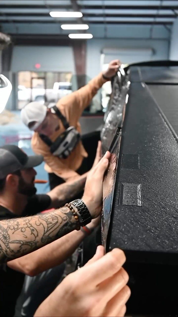 Workers applying protective wrap to a large black object in a workshop