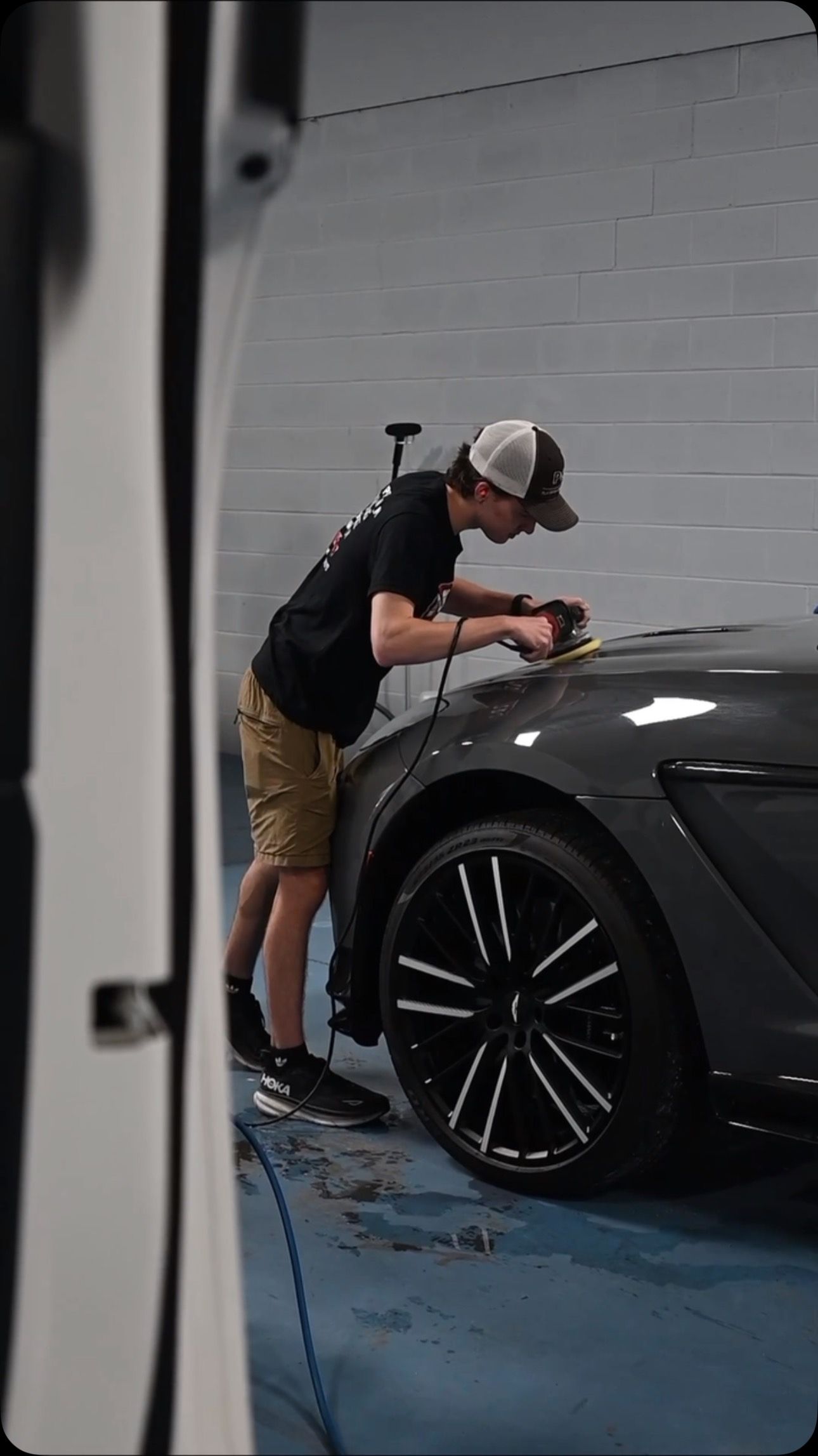 Mechanic polishing a dark gray car’s front fender in a garage