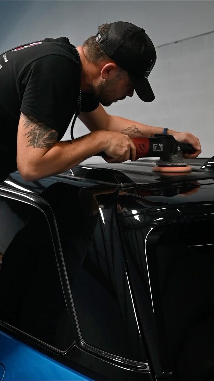 Man polishing a black car with a handheld buffer in a garage