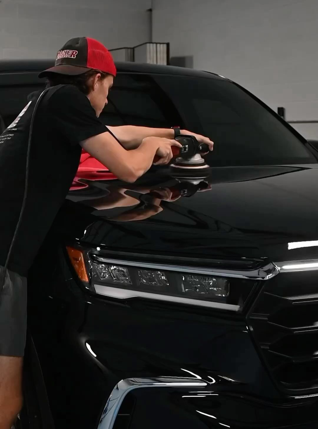 Person cleaning the windshield of a black SUV in a garage