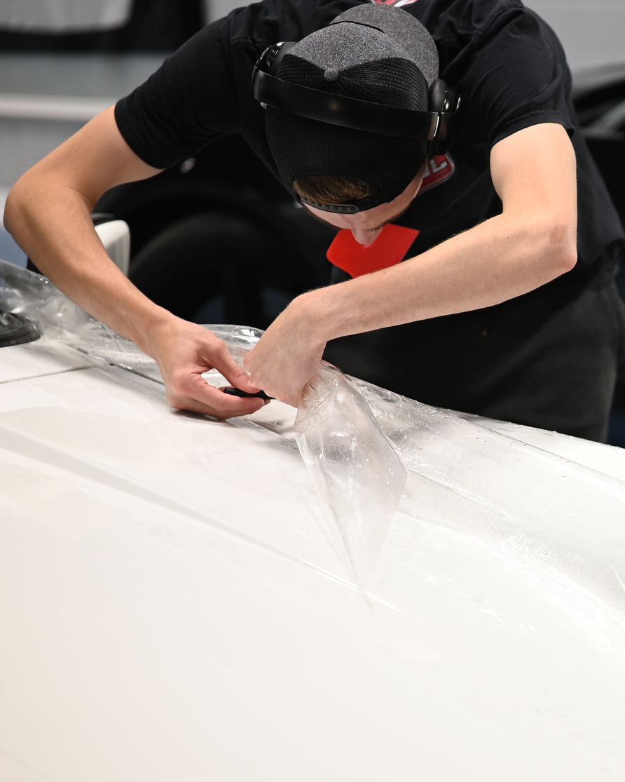 Person in a black shirt carefully cutting white fabric on a table with a red tool