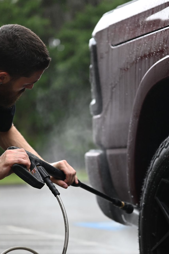 Person pressure-washing a maroon vehicle in the rain