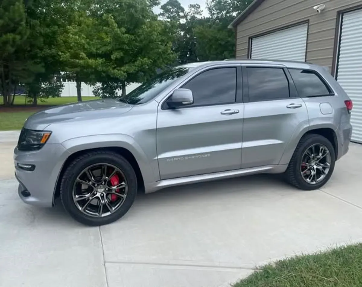 A silver grand cherokee is parked in a driveway next to a garage.