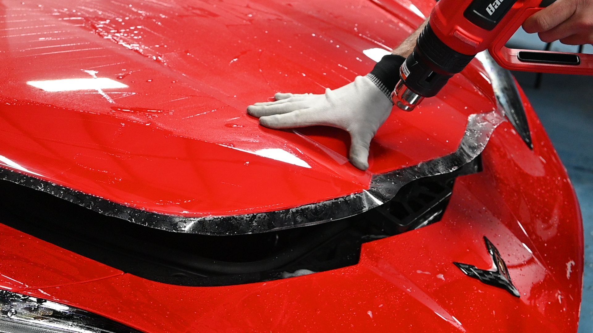 A person is wrapping a red car with PPF.