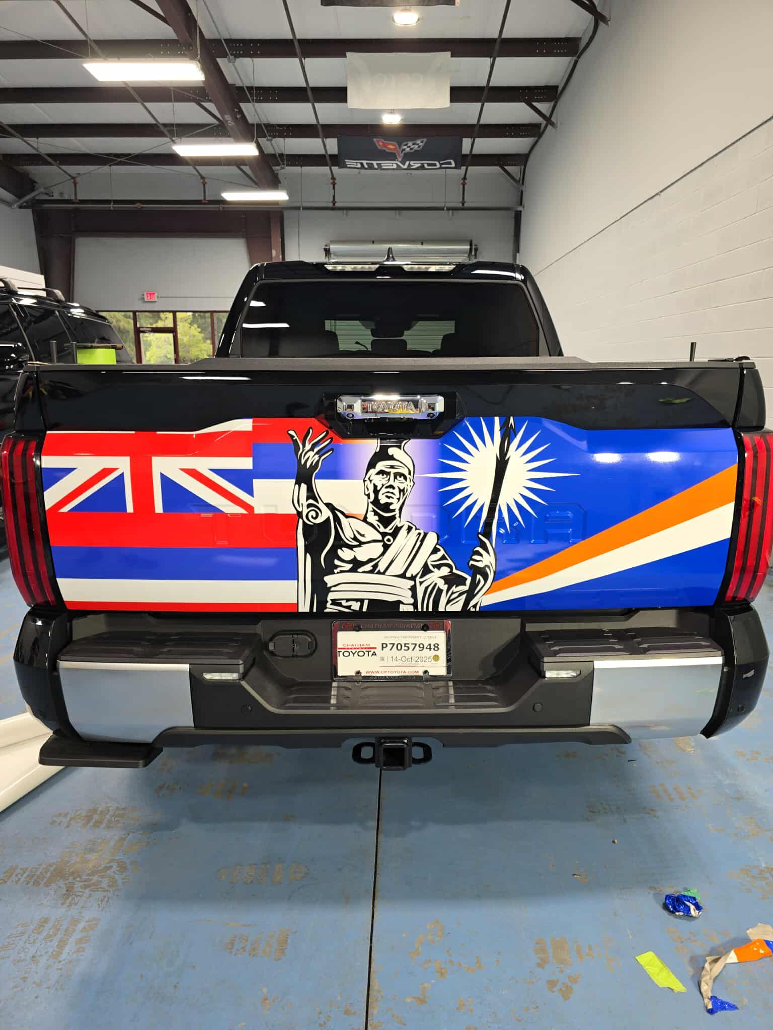 Pickup truck rear with colorful flag wrap in a garage; black, red, blue, and white design.