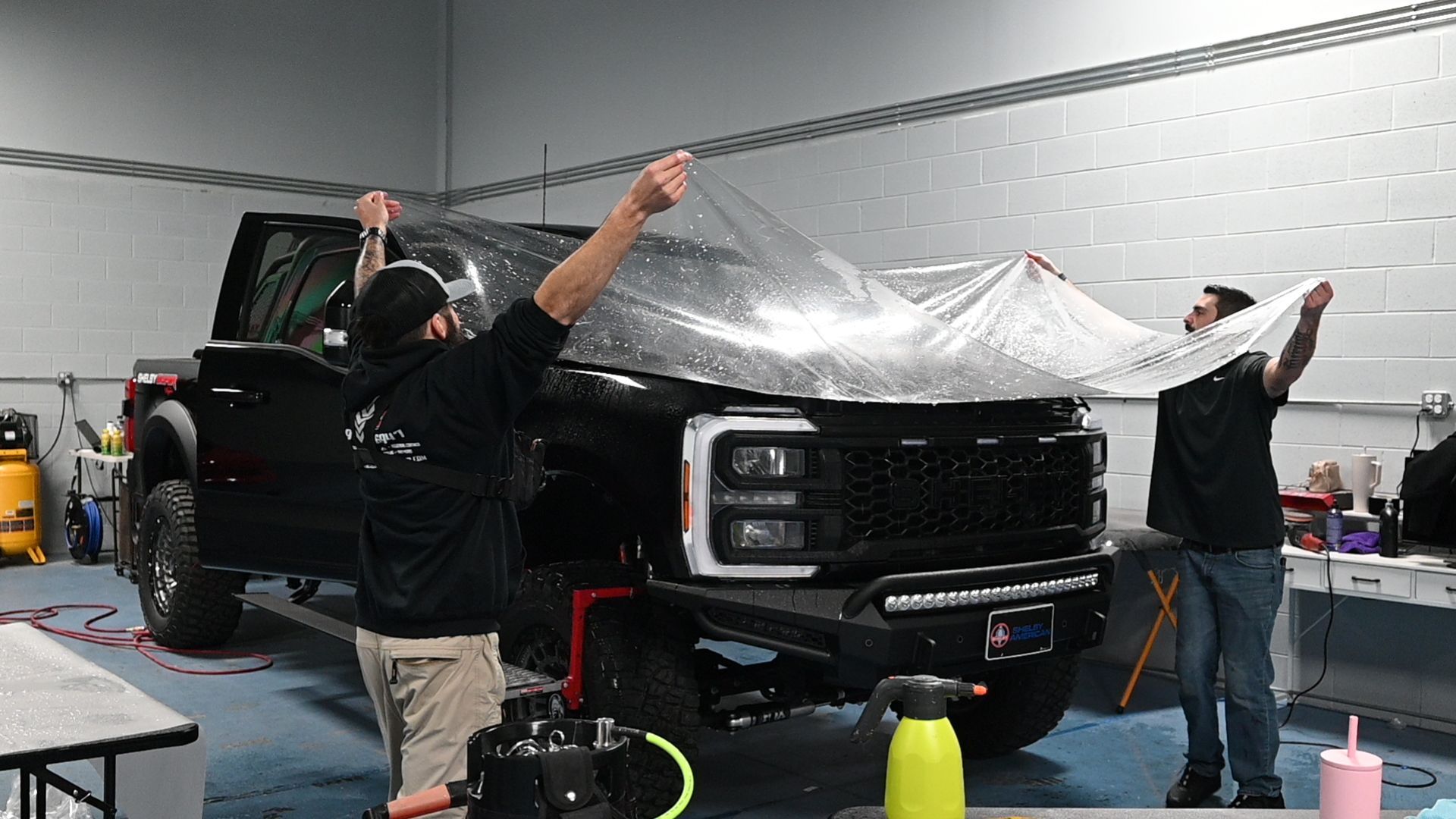 Detailing technician installing clear film on vehicle bumper – answering the question: is paint protection film worth it for daily drivers.