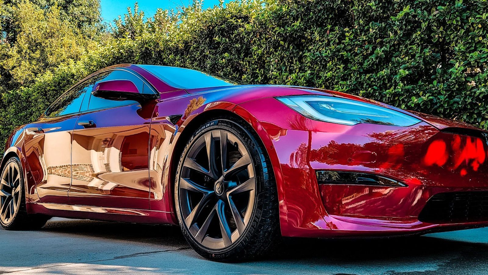 Red sports car with glossy paint parked on a sunlit road, trees in the background