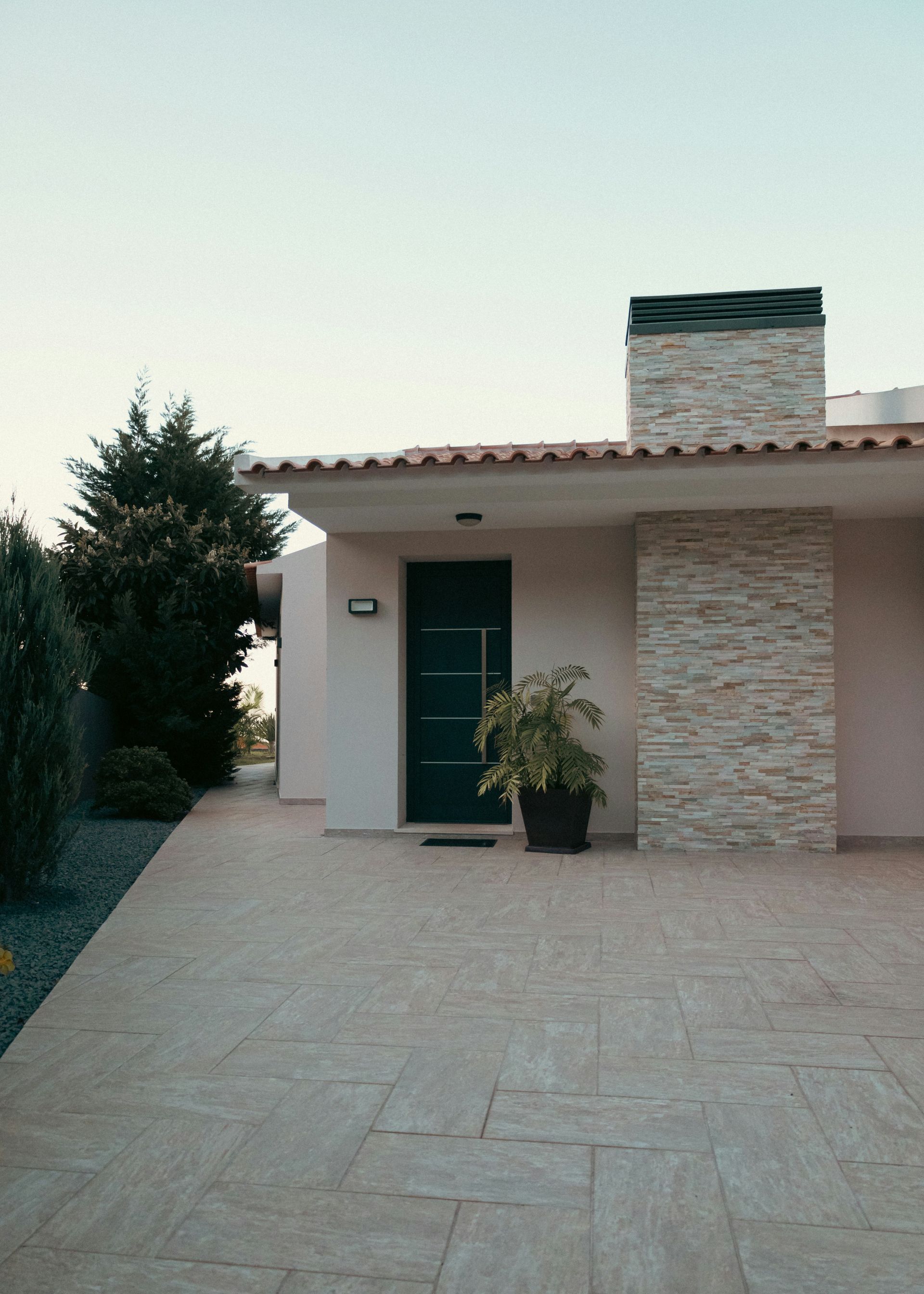 Small modern house with a tiled driveway, green front door, and potted plant at dusk