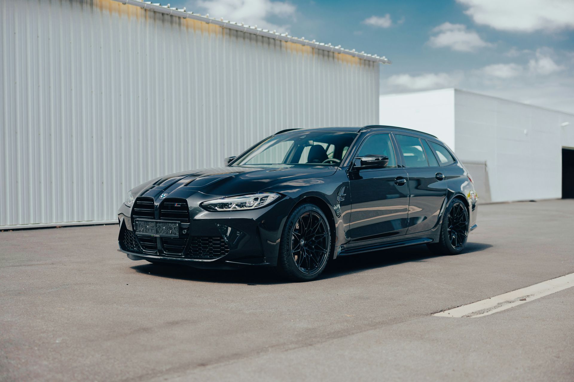Black BMW sedan parked in an industrial lot beside a white warehouse