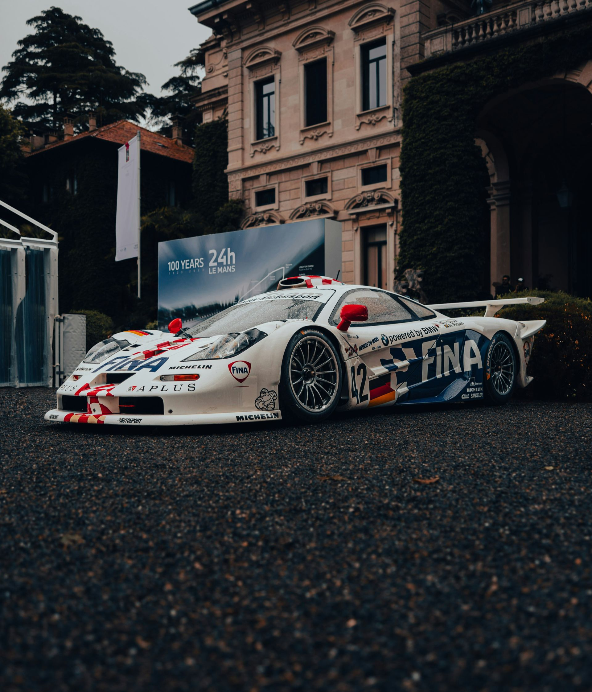 White drift car with red decals parked on wet pavement in front of an old building