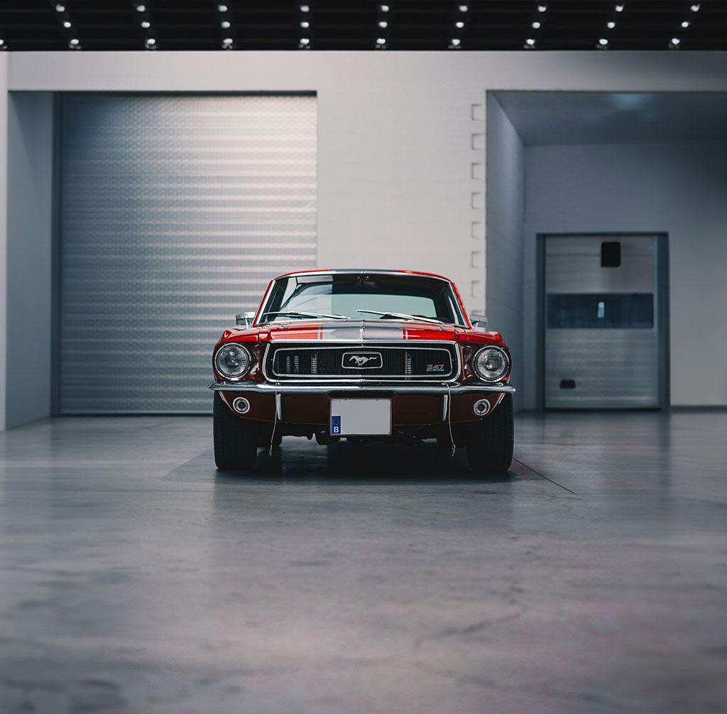Red classic muscle car centered in a modern showroom with gray walls and bright overhead lights