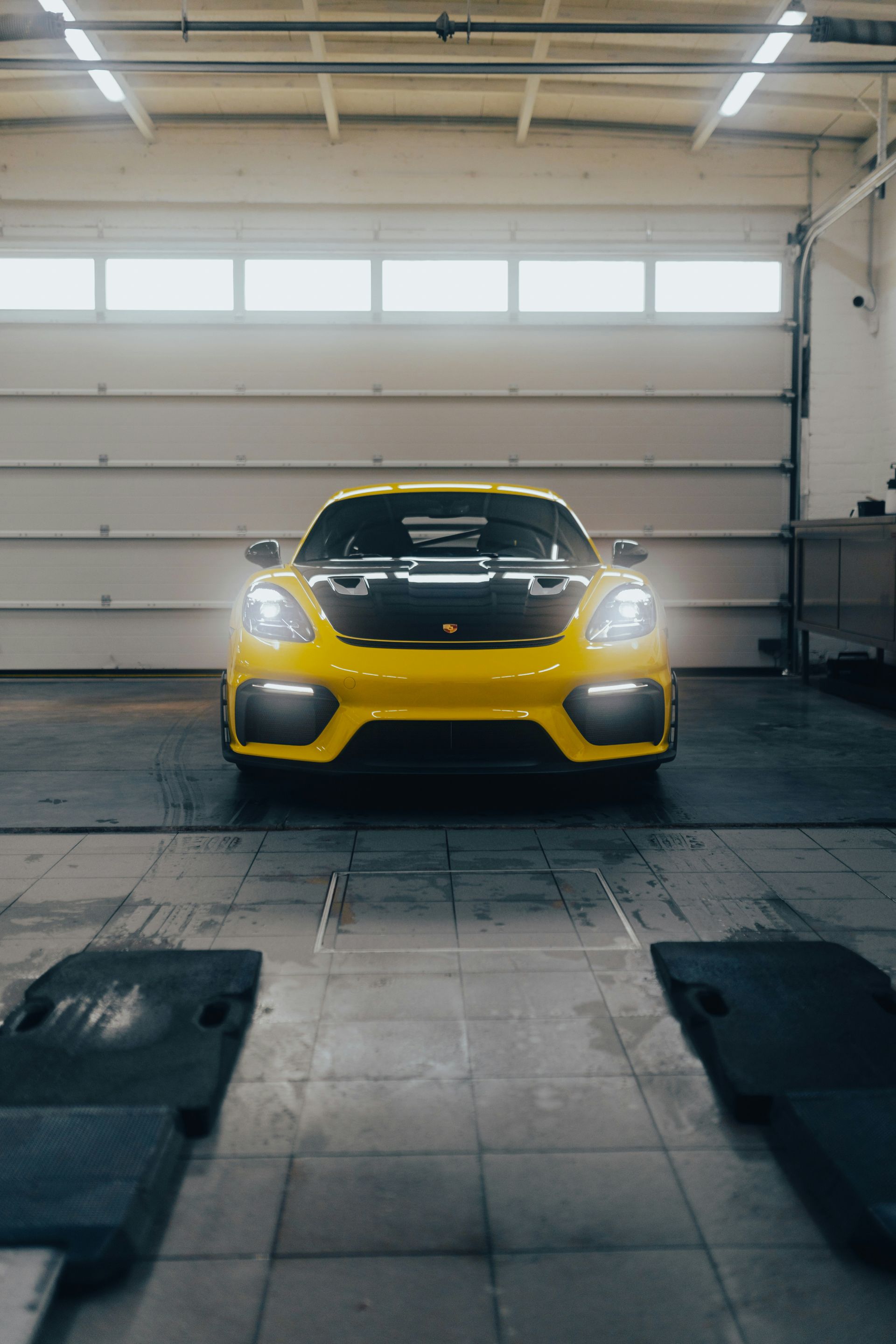 Yellow sports car parked in a garage, facing forward with headlights on.