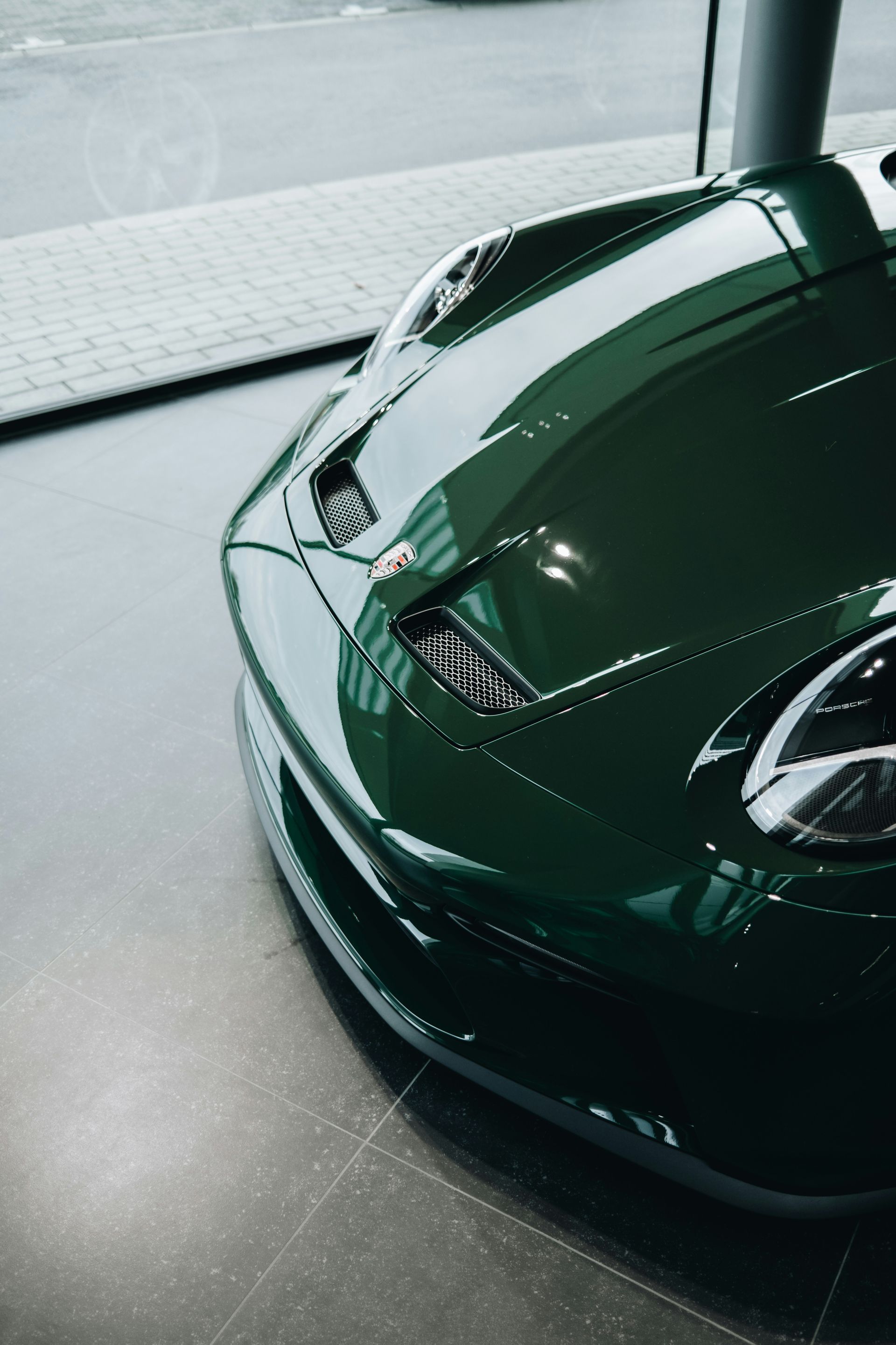 Front view of a dark green sports car in a showroom, with a glossy hood and headlight visible
