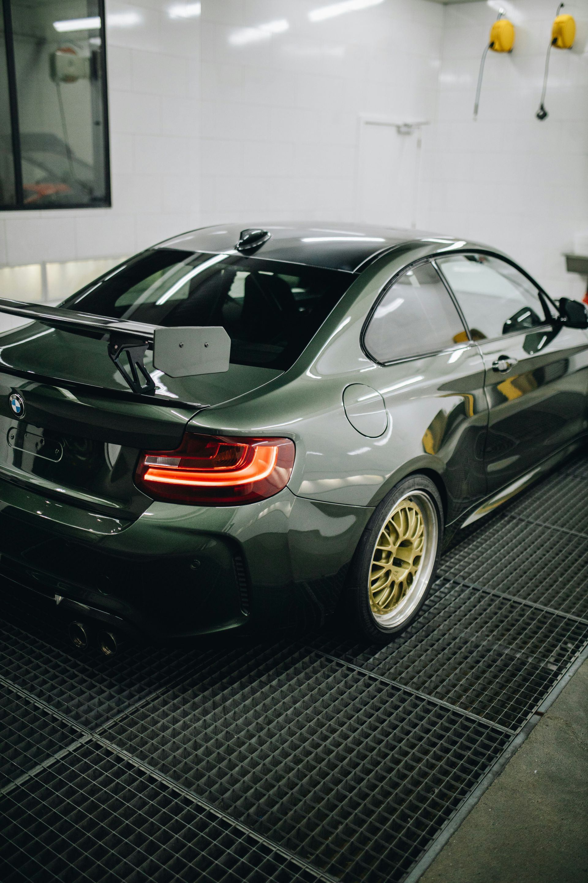 Gray sports coupe with gold wheels in a car wash bay, rear view