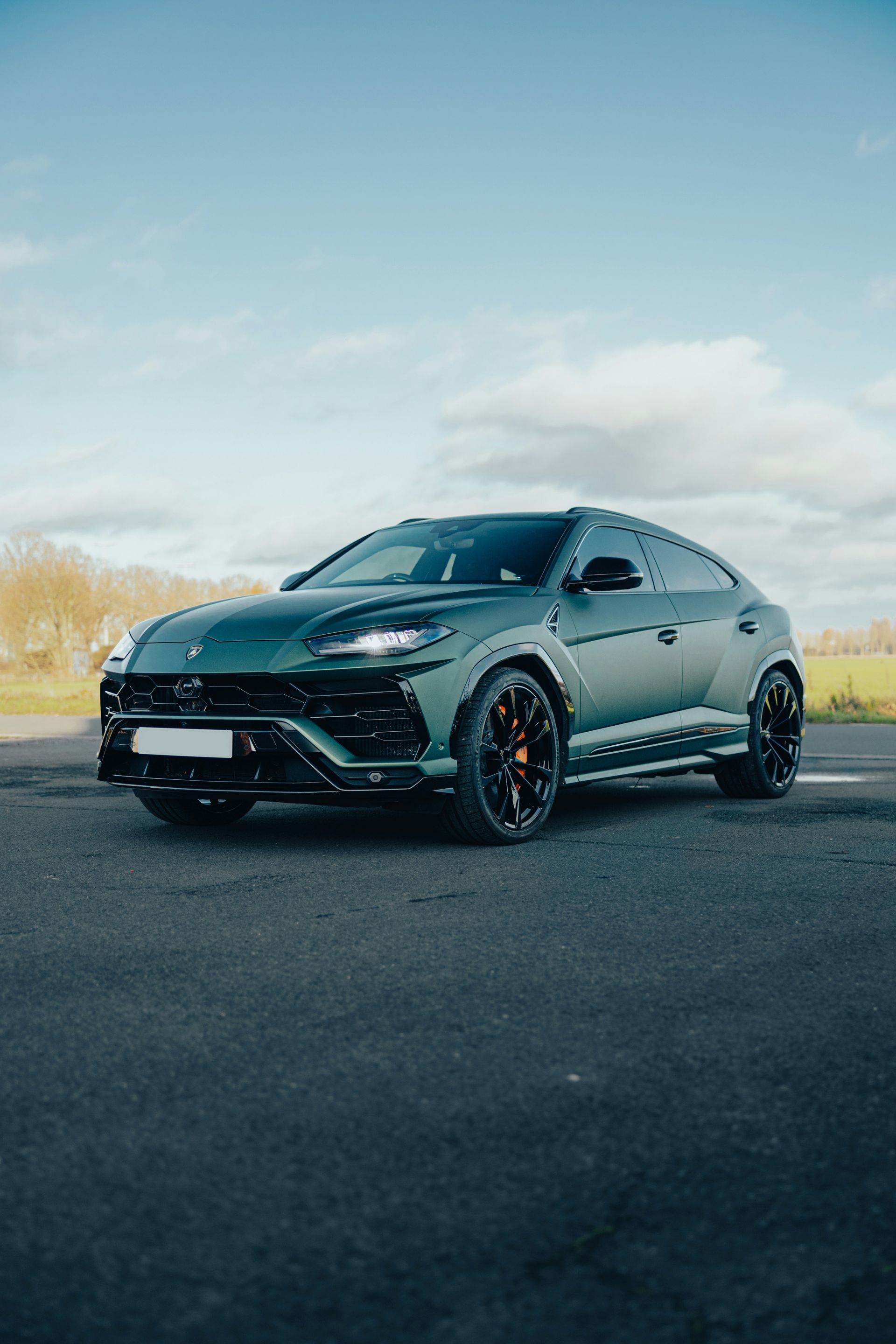 Dark green sports car parked on pavement under a blue sky.