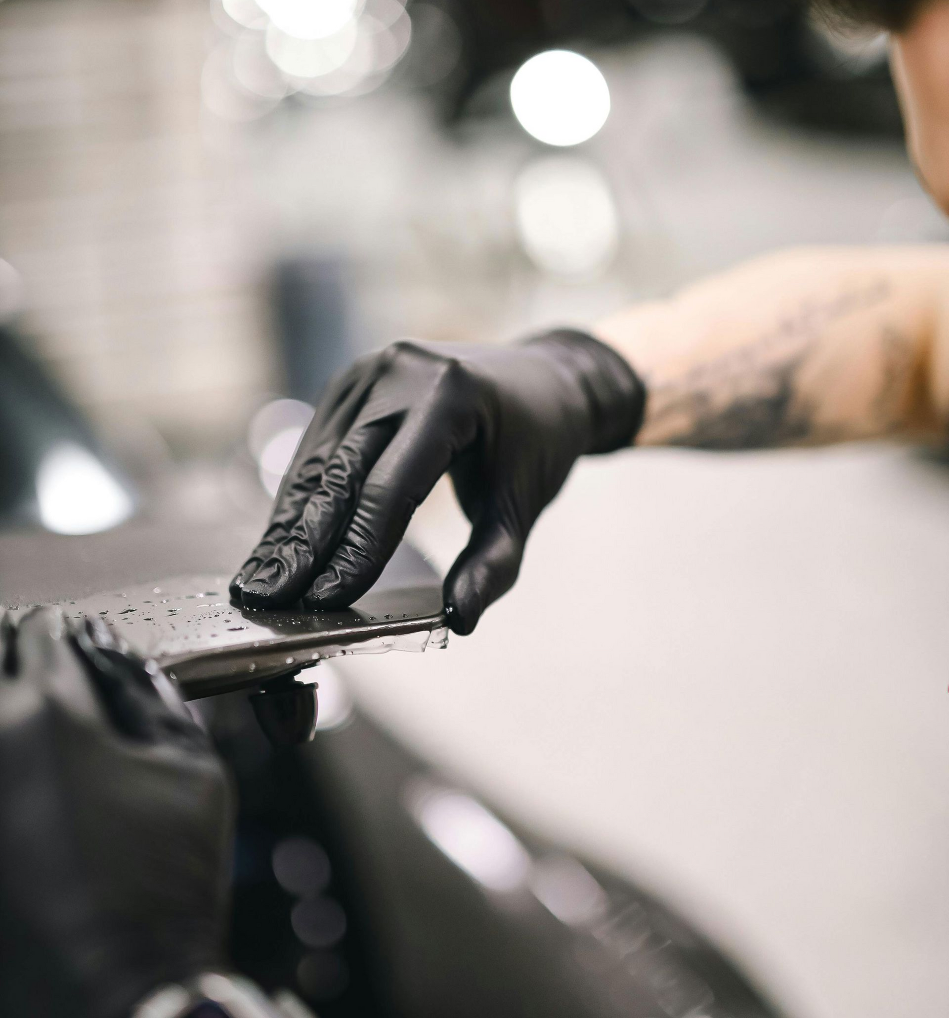 Black-gloved hand wiping a tattoo machine with a cloth in a studio