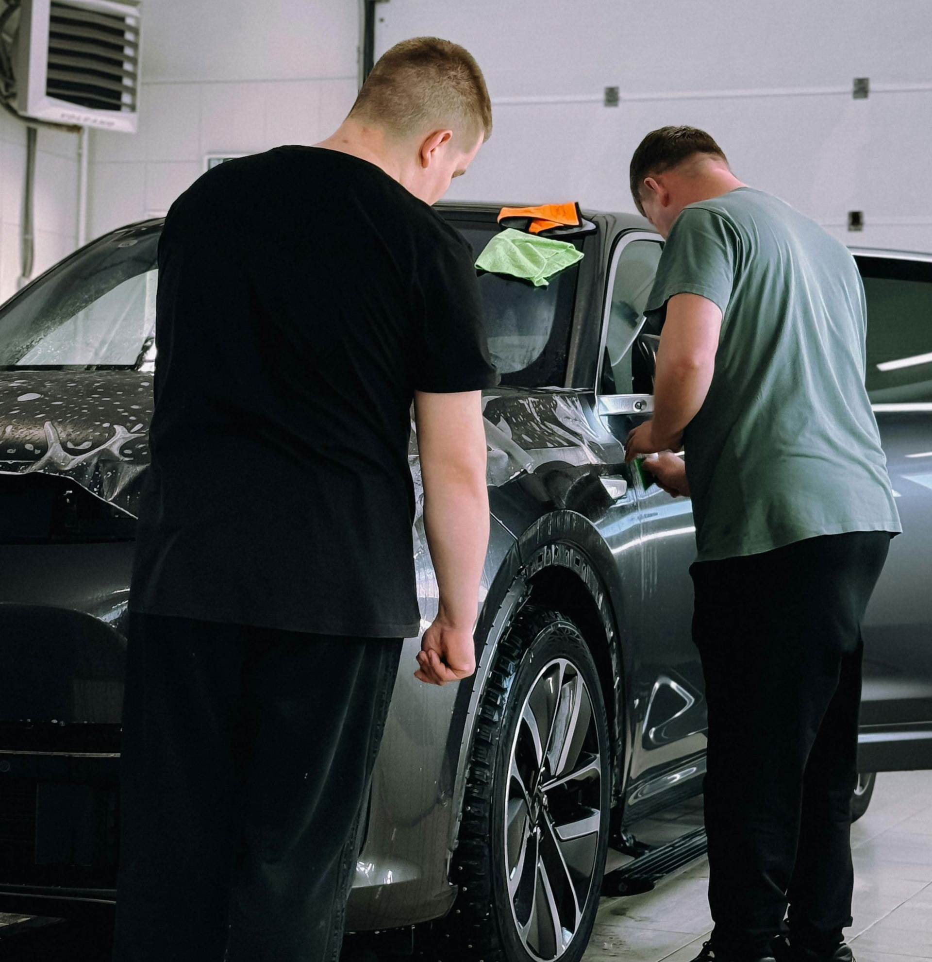 Two people washing a black car indoors at a detailing shop
