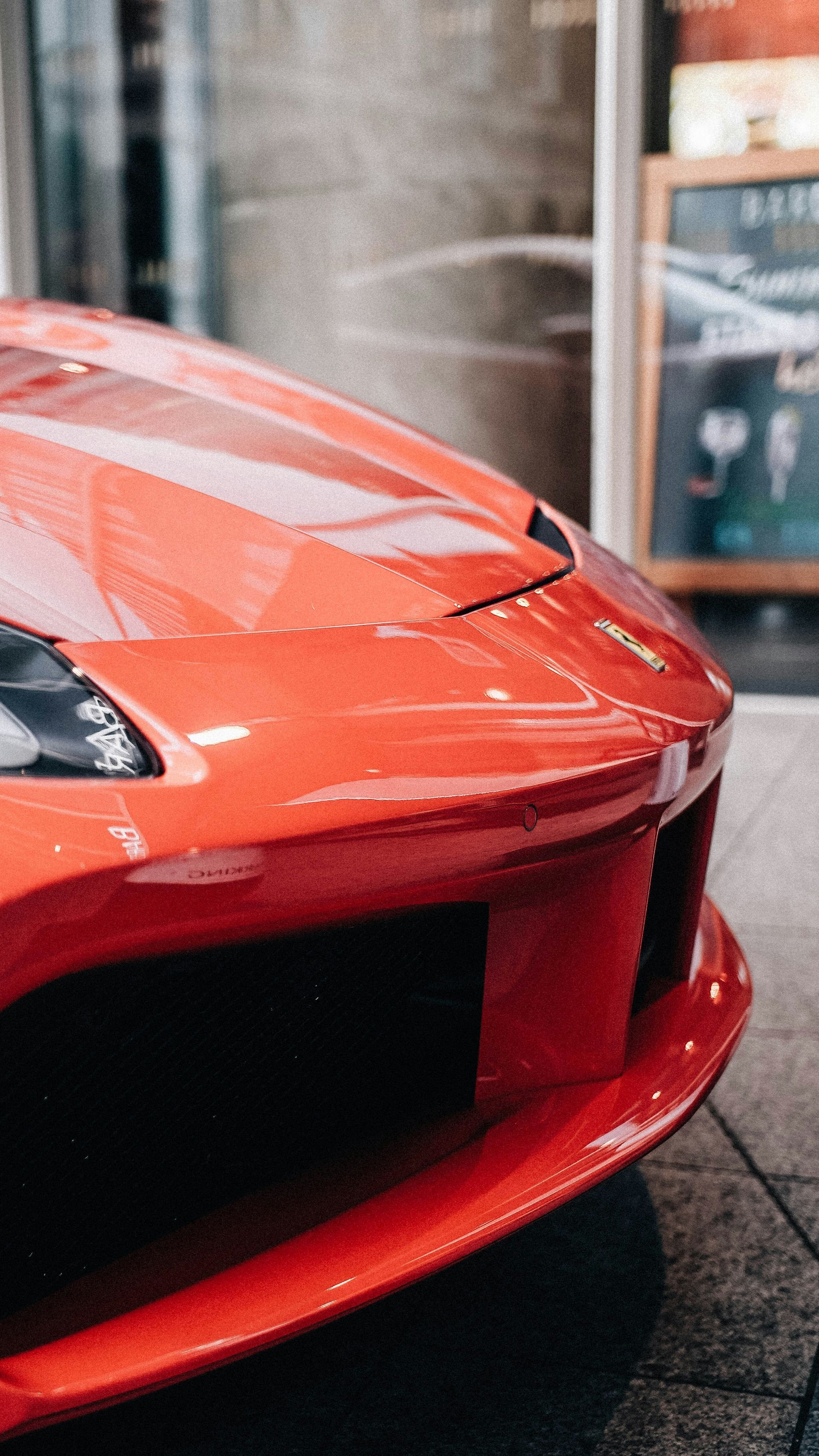 Close-up of the front of a red sports car with a black grille, parked outdoors near a storefront.