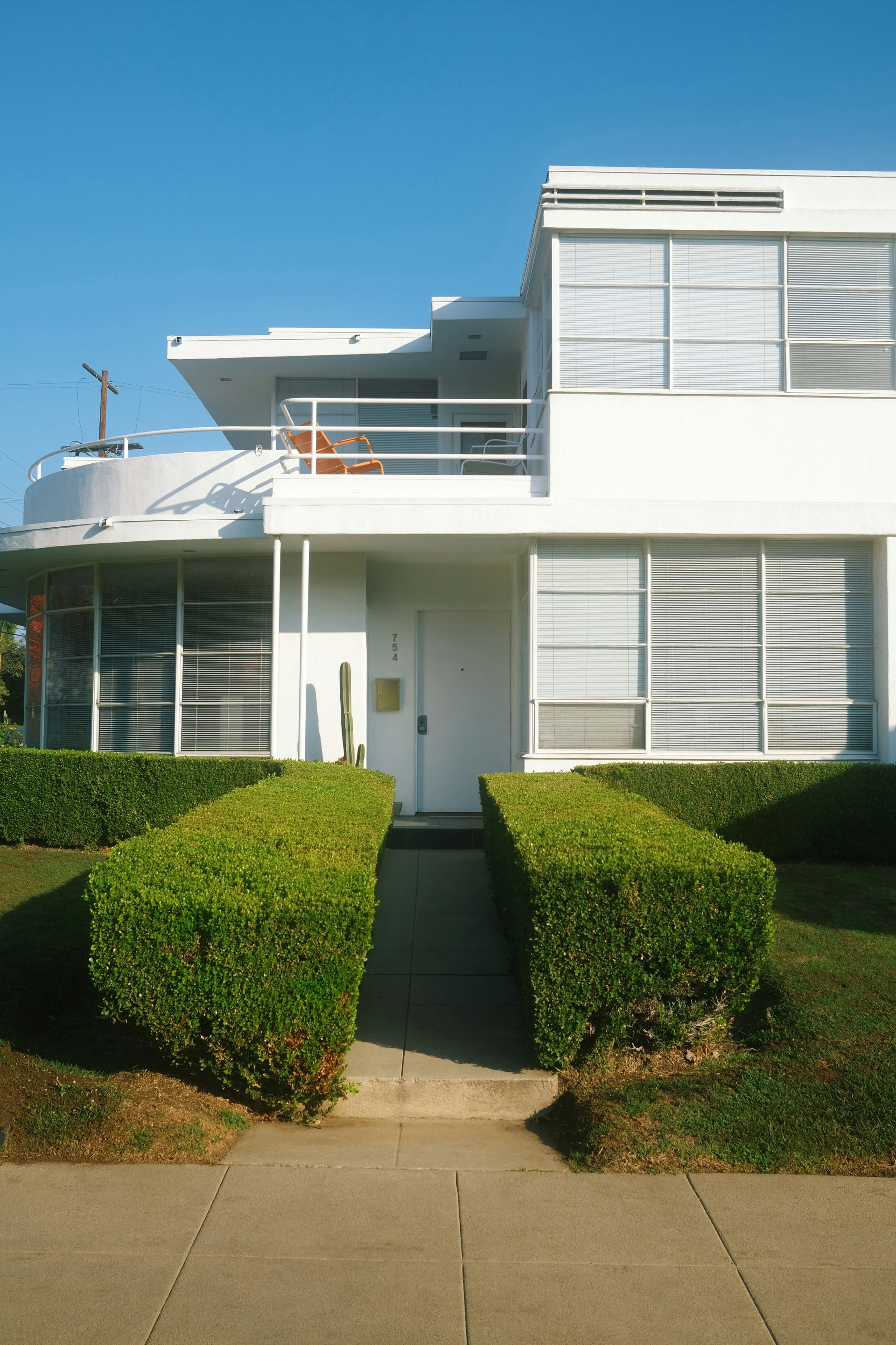 Modern white townhouse with hedges and a walkway under a clear blue sky