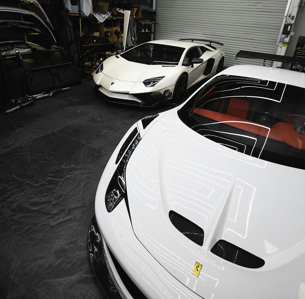 Two white sports cars parked in a garage, one with a red interior and Ferrari badge.