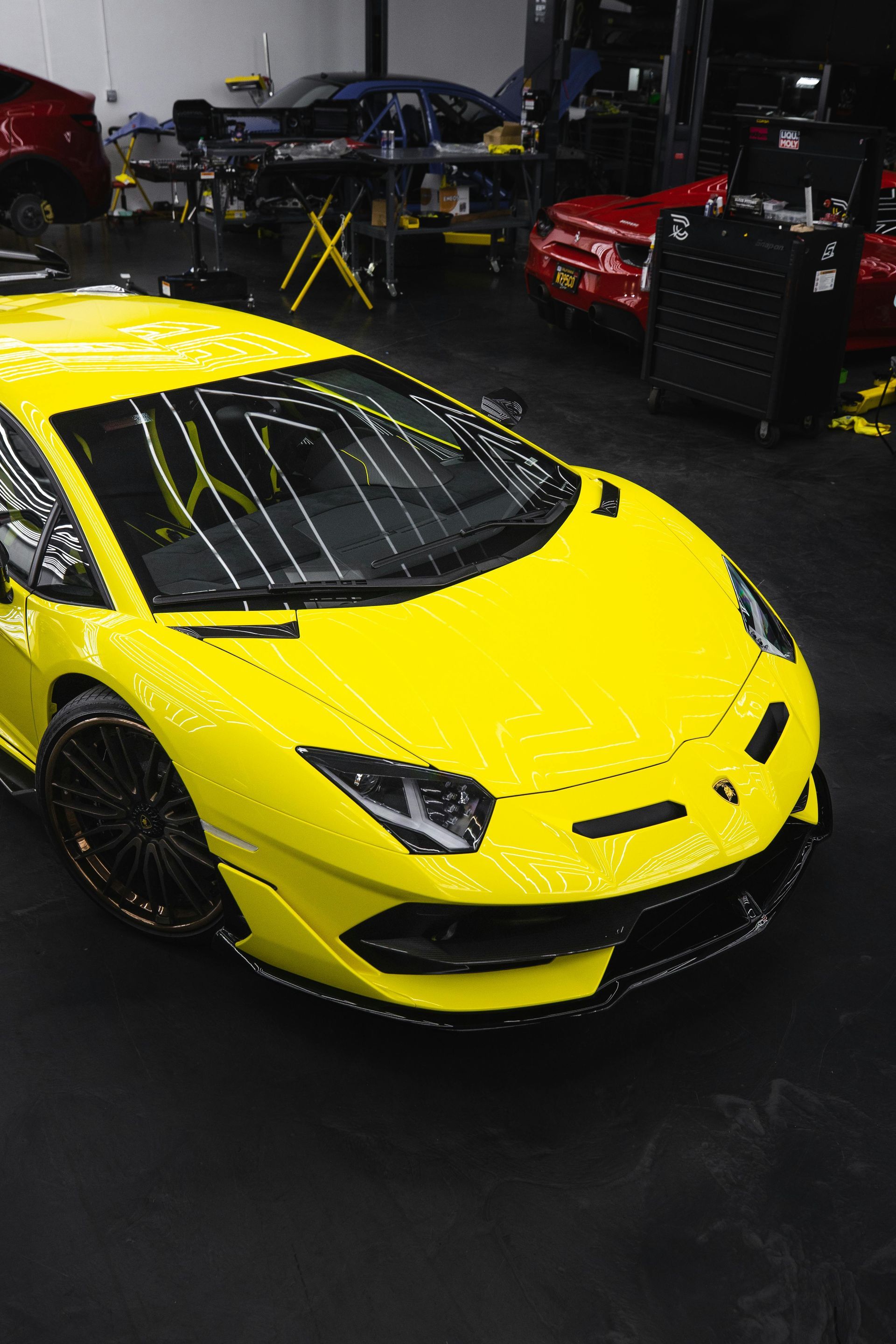 Yellow sports car in a dim garage with other cars and tools in the background