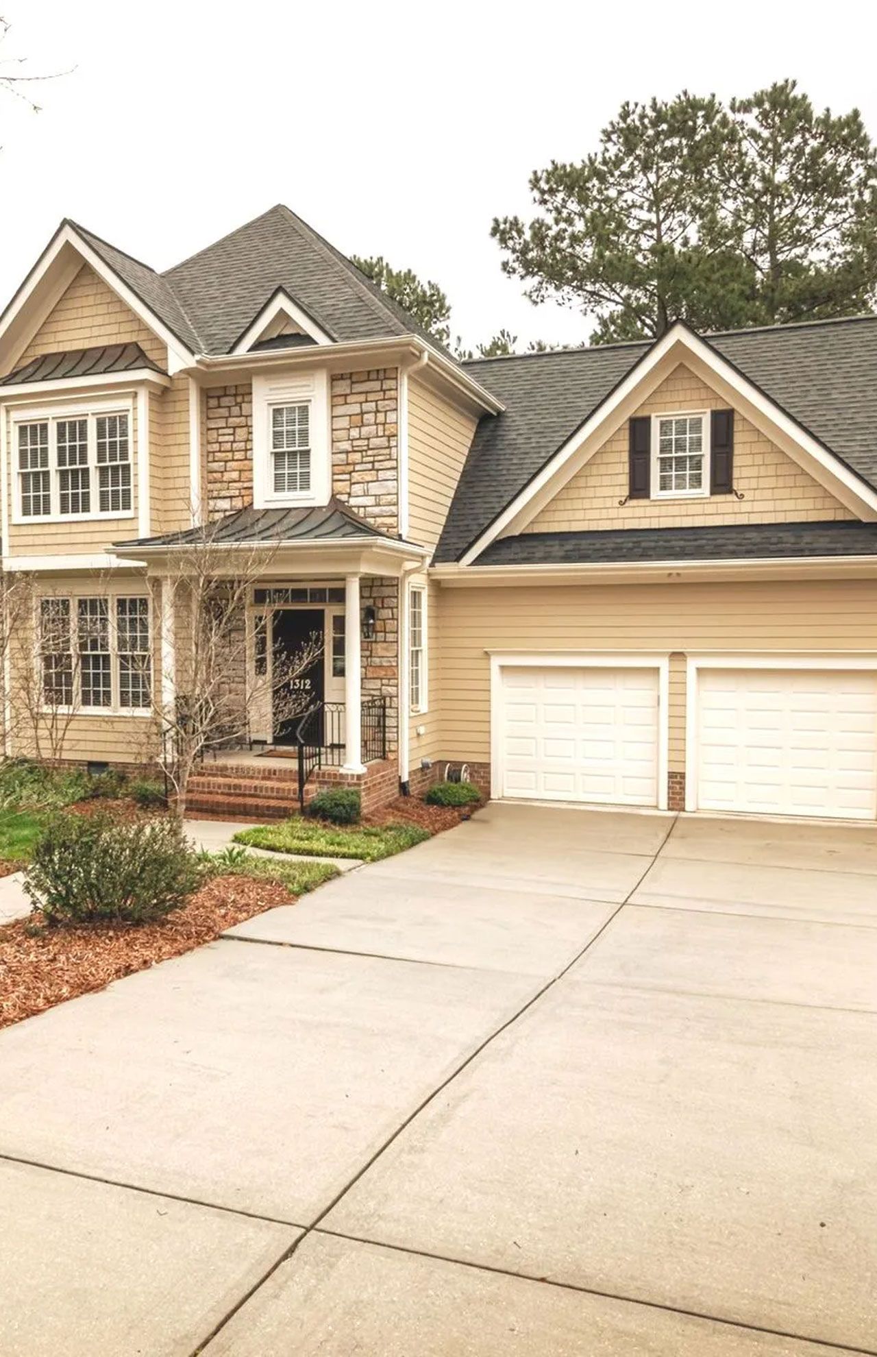 Two-story beige house with a front porch, double garage, and large driveway