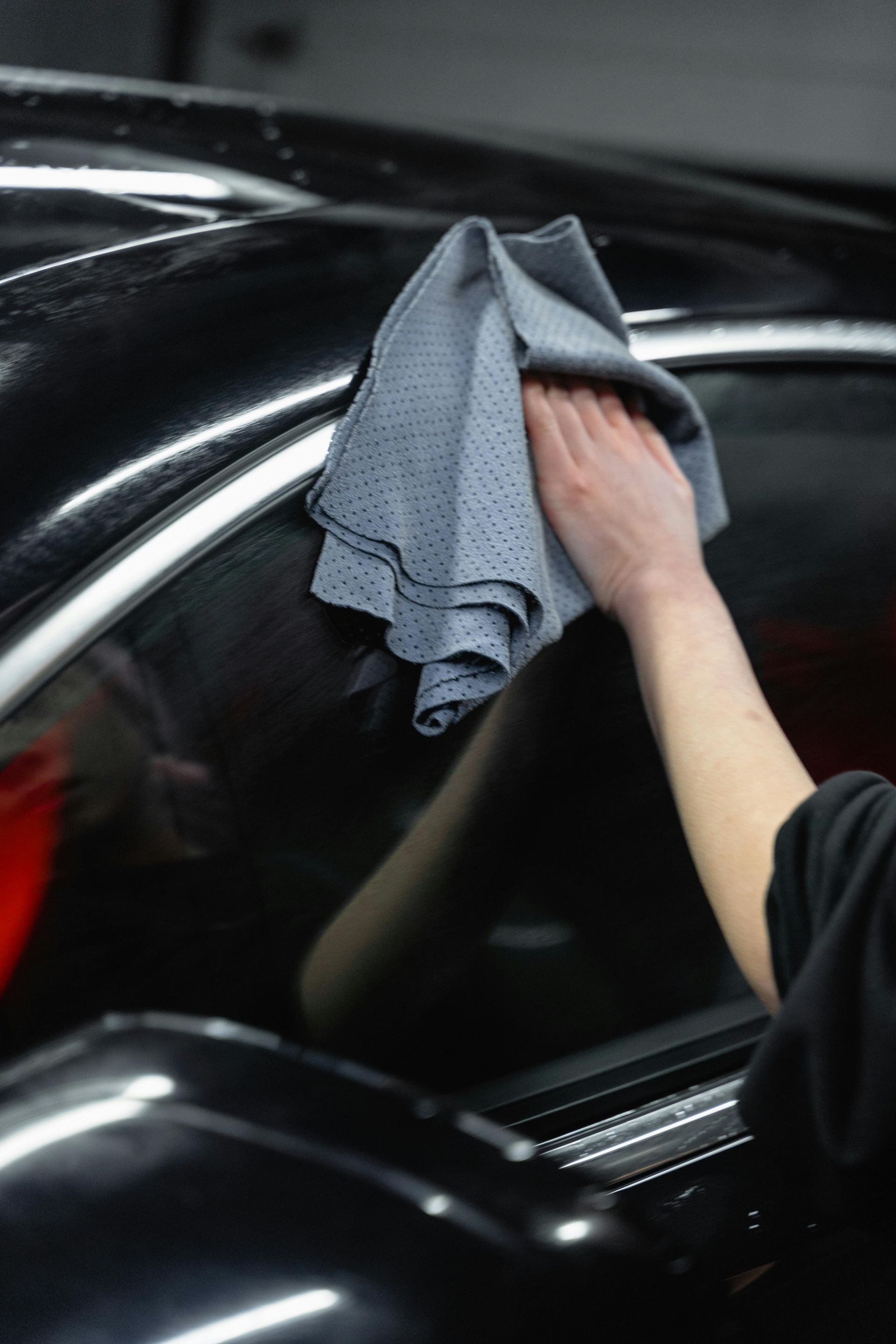 Hand wiping a black car with a gray cloth during cleaning