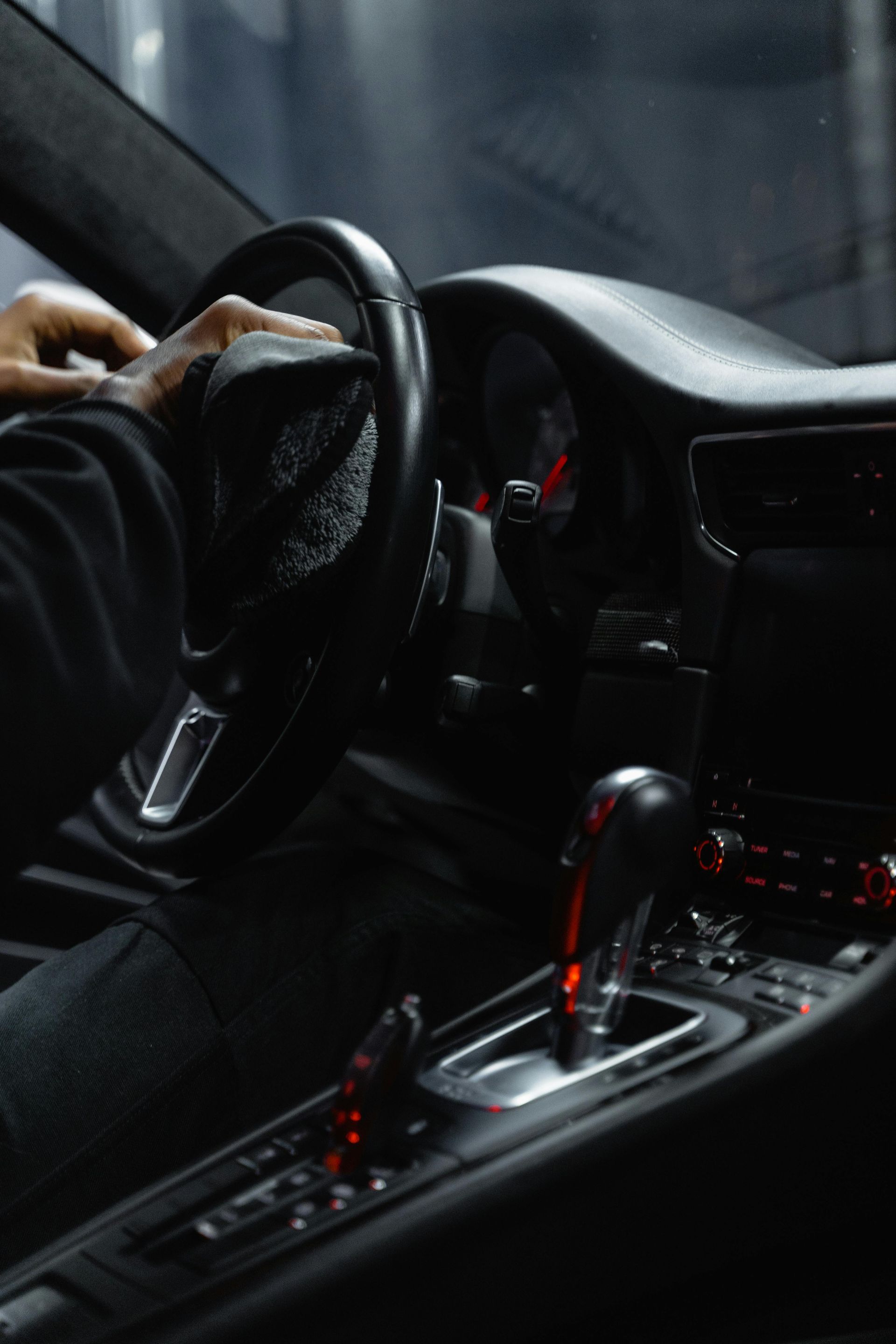 Driver’s hands on a steering wheel in a dark car interior, with the center console and gear shift lit red.