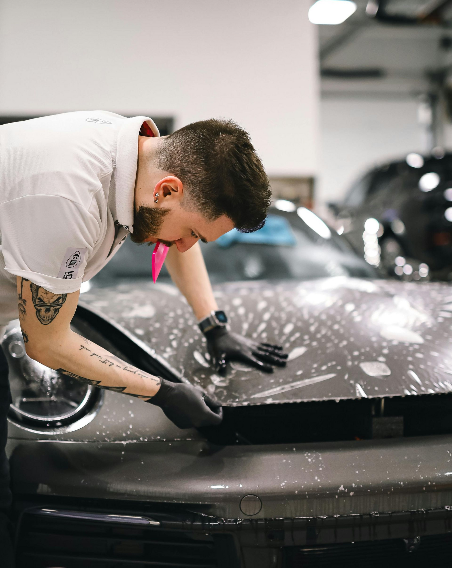 Mechanic in black gloves polishing a car hood in a garage