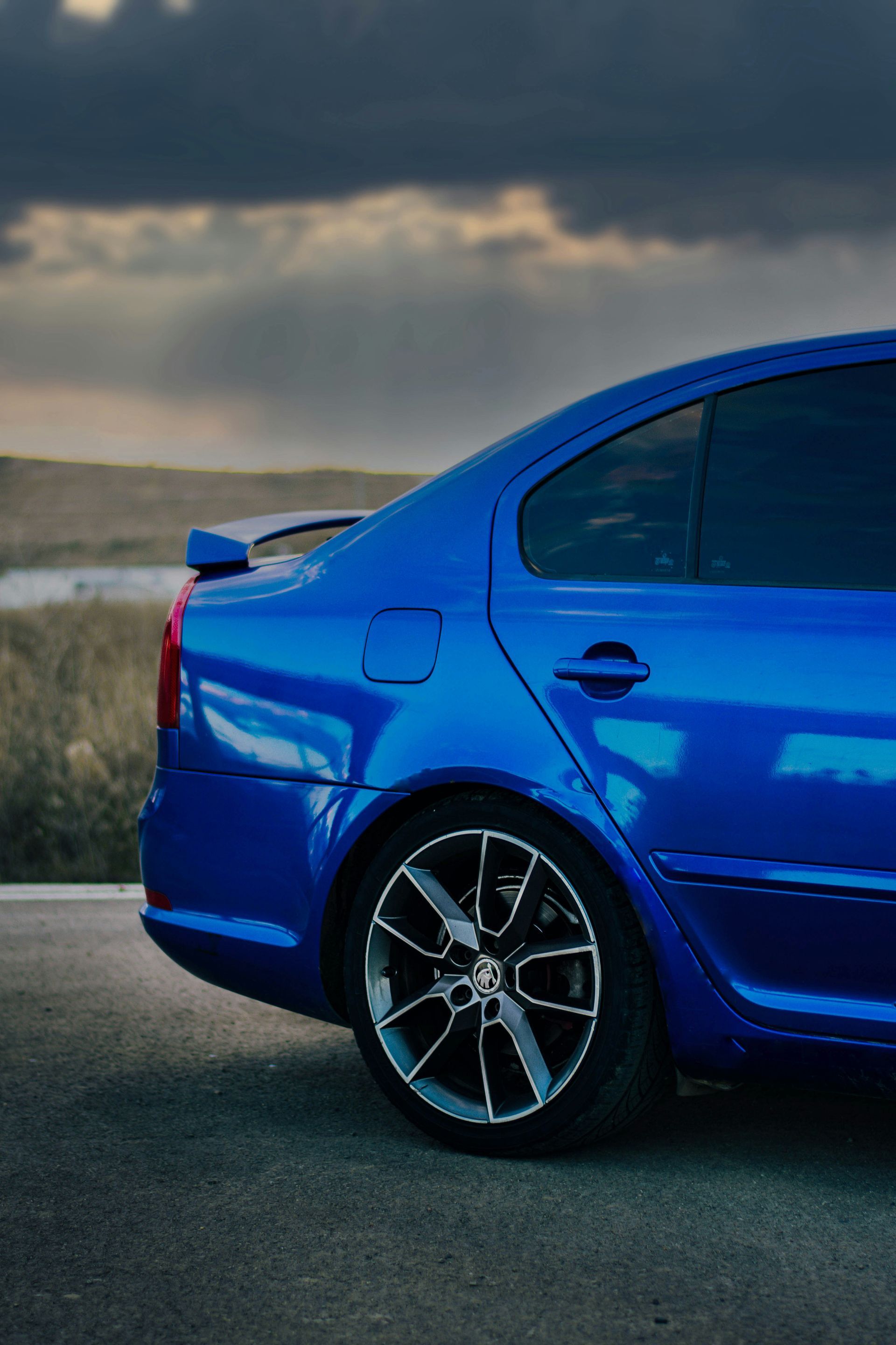 Blue sports sedan parked on a roadside under a cloudy sky.