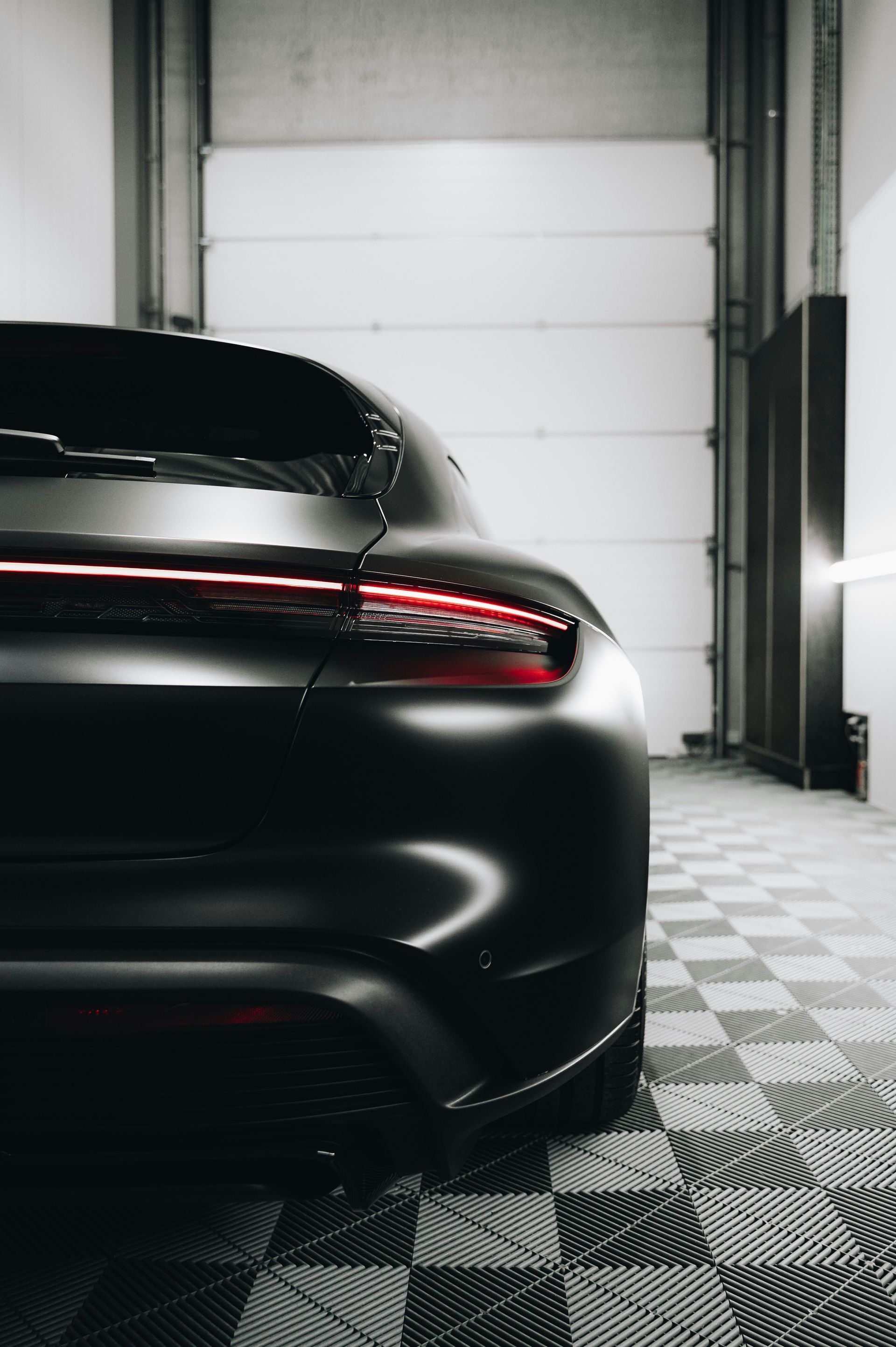 Rear view of a black sports car parked in a garage with a white door and checkered floor