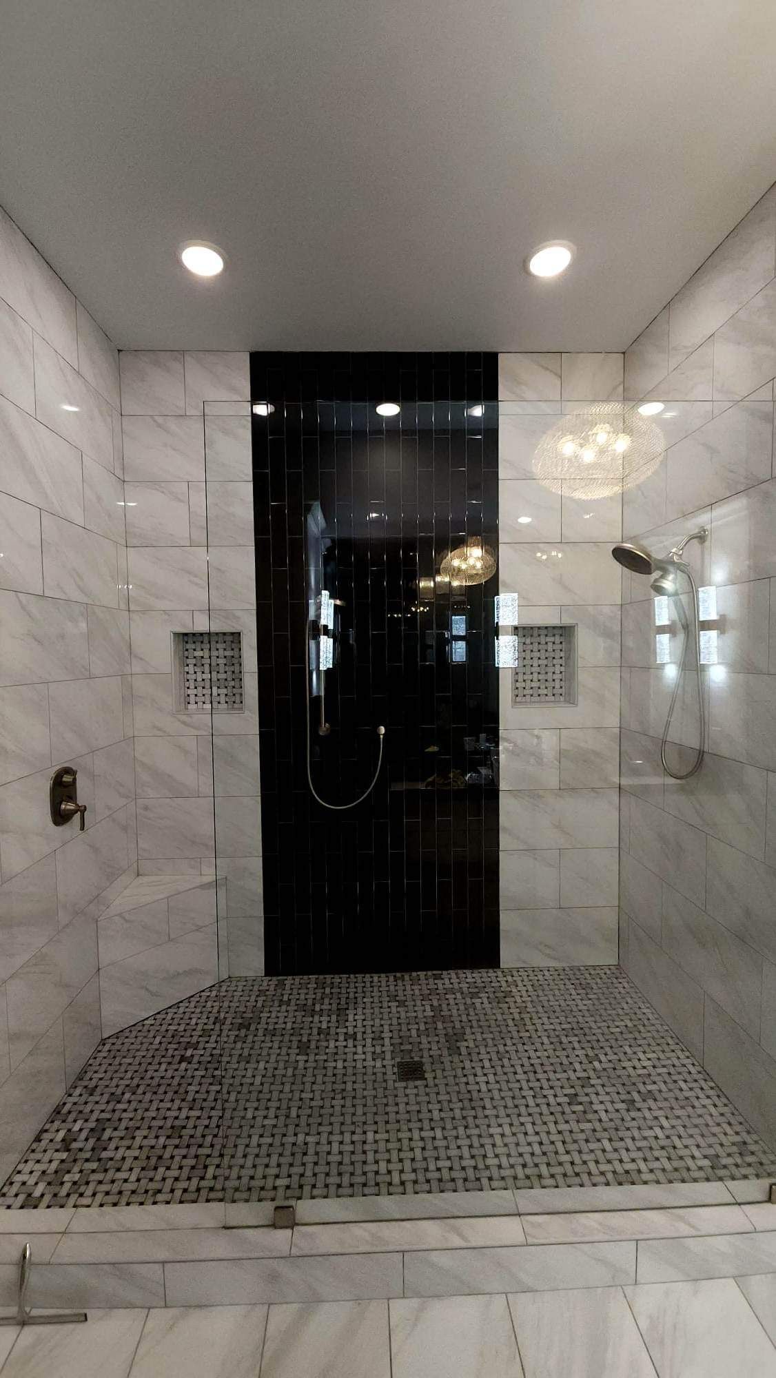 Modern shower with marble walls, black accent panel, glass door, and pebble floor.