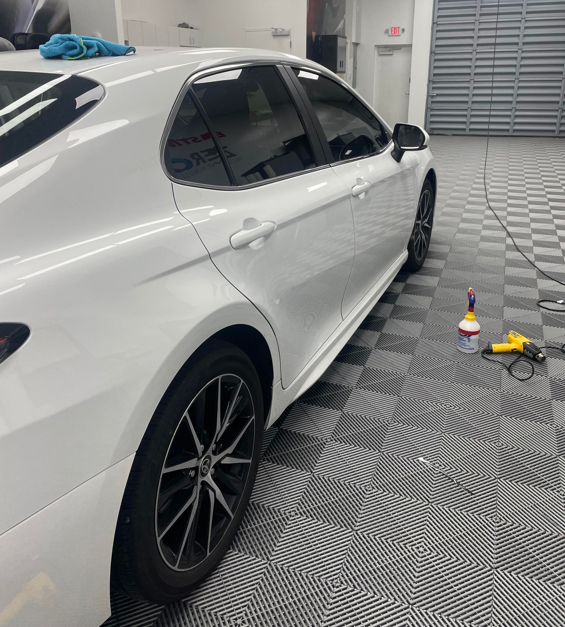 White sedan in a detailing bay with cleaning supplies on patterned floor tiles.