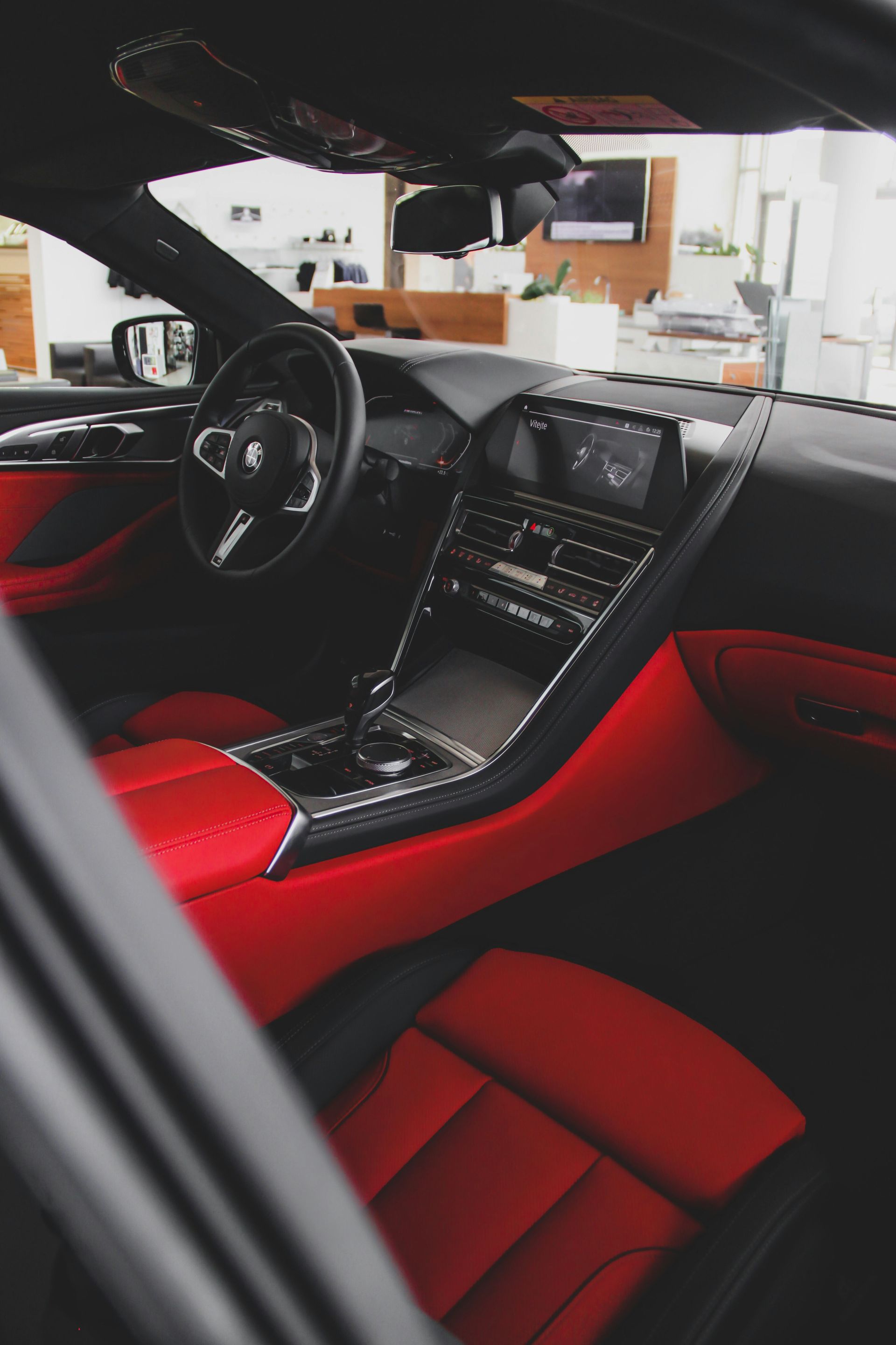 Red leather car interior with a black steering wheel and center console, viewed from the passenger side.