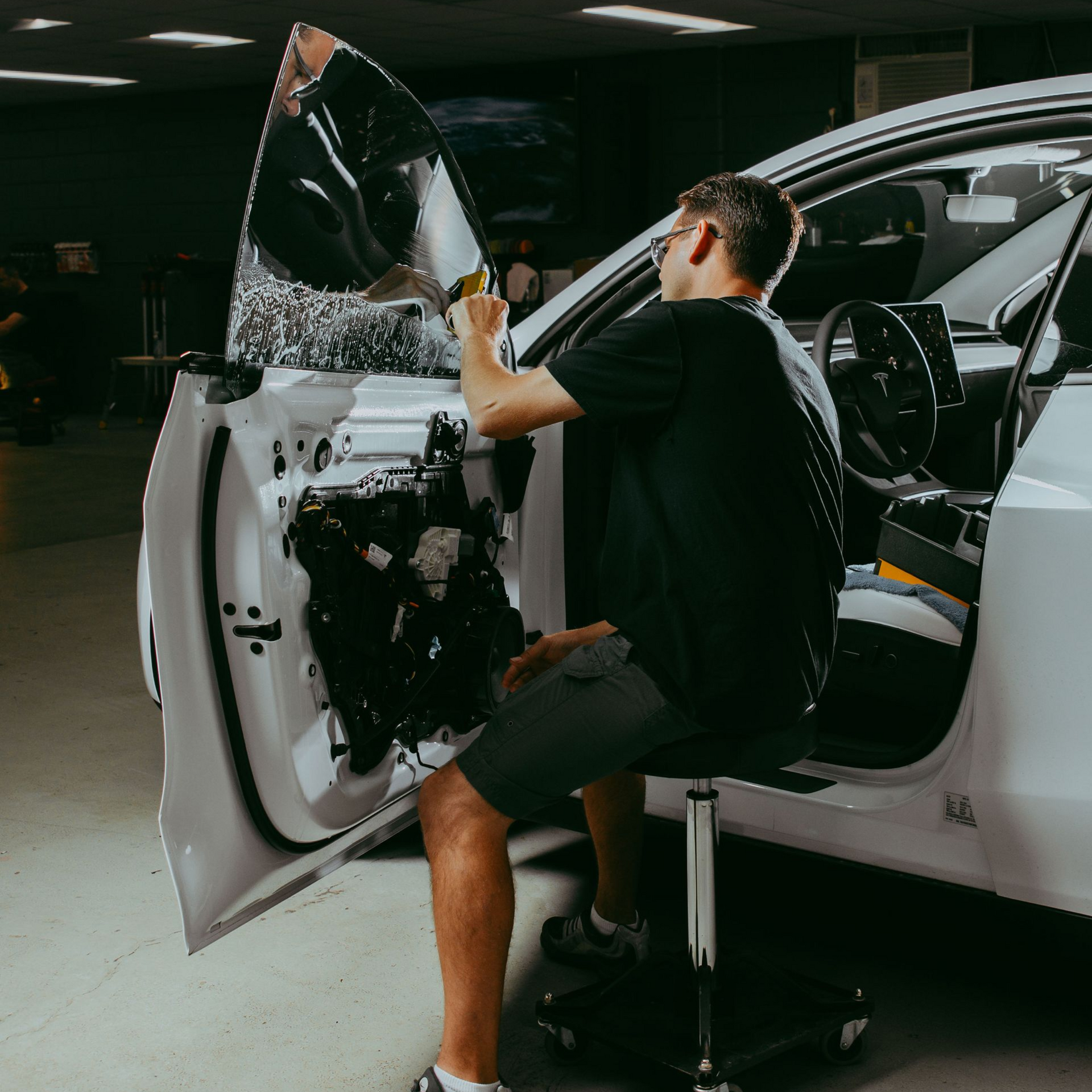 Car wrap installer applying vinyl film to a white car door in a workshop