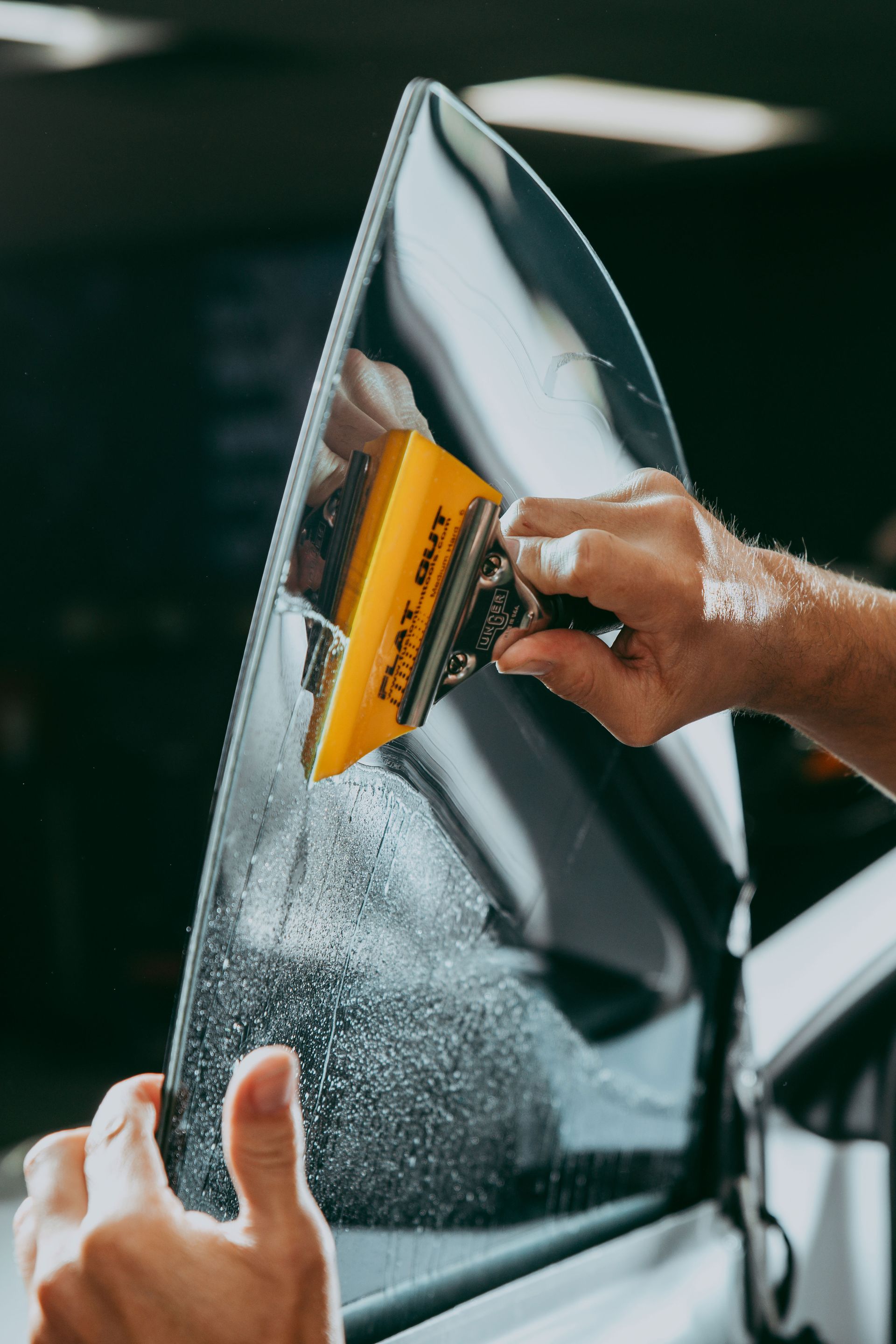 Hand applying a yellow squeegee to a reflective film on a window or panel