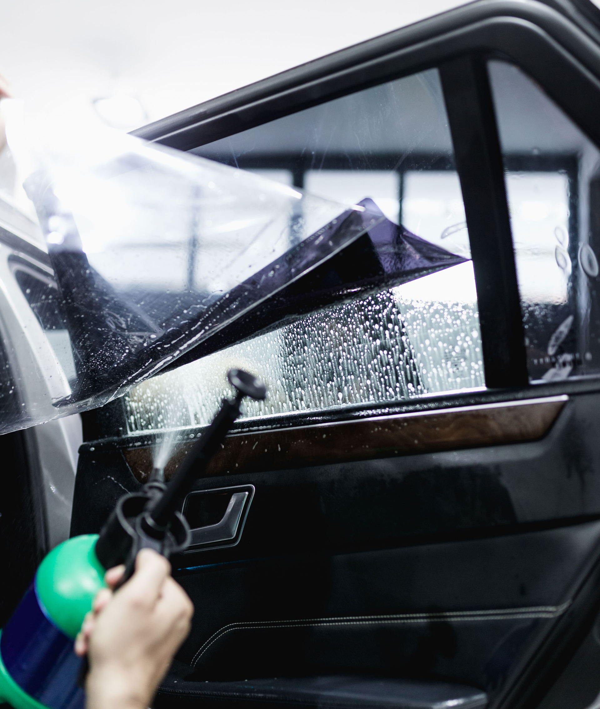 Person spraying water at a car window as a black windshield wiper lifts rainwater