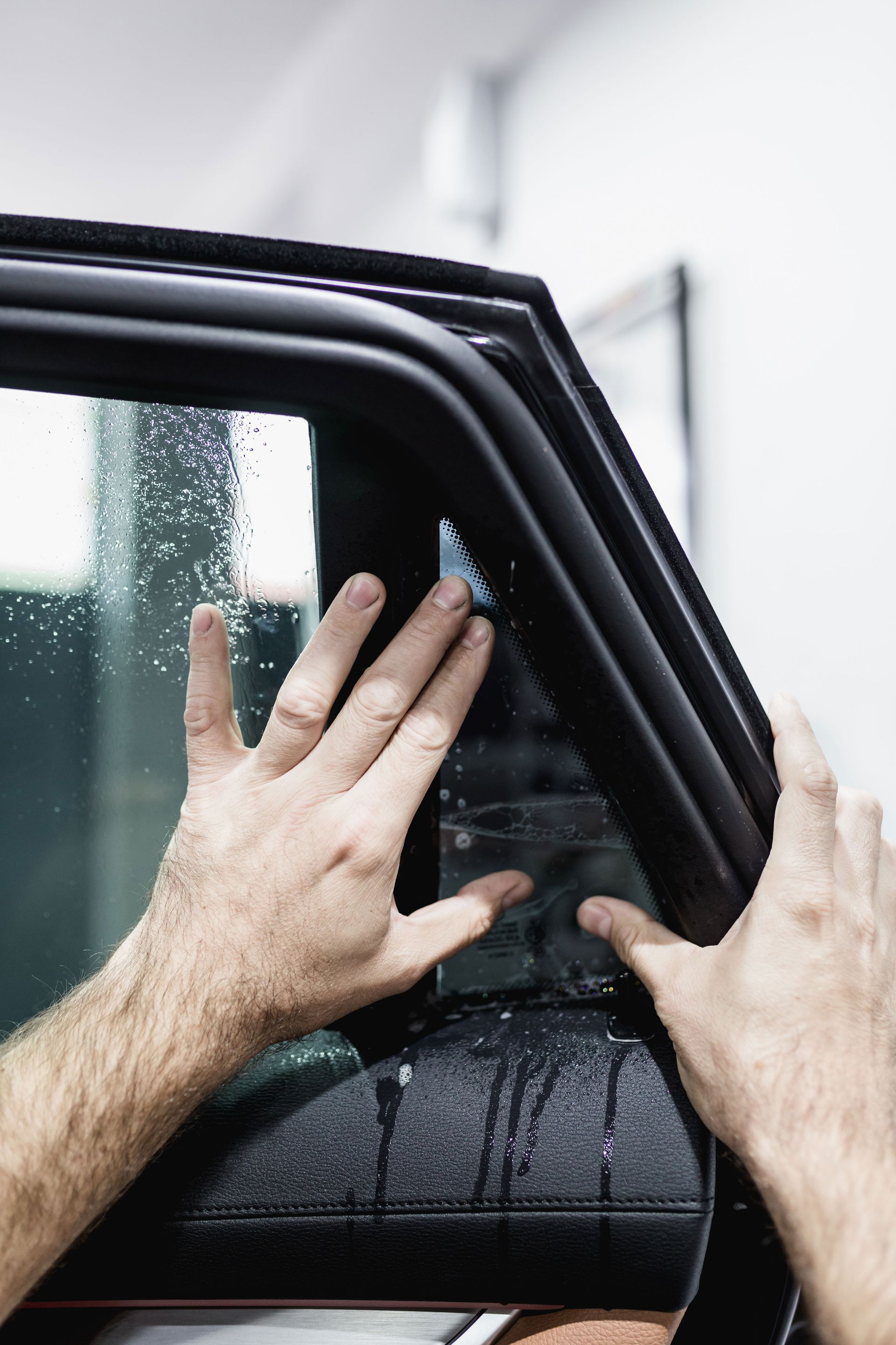 Hands cleaning a black car window in the rain