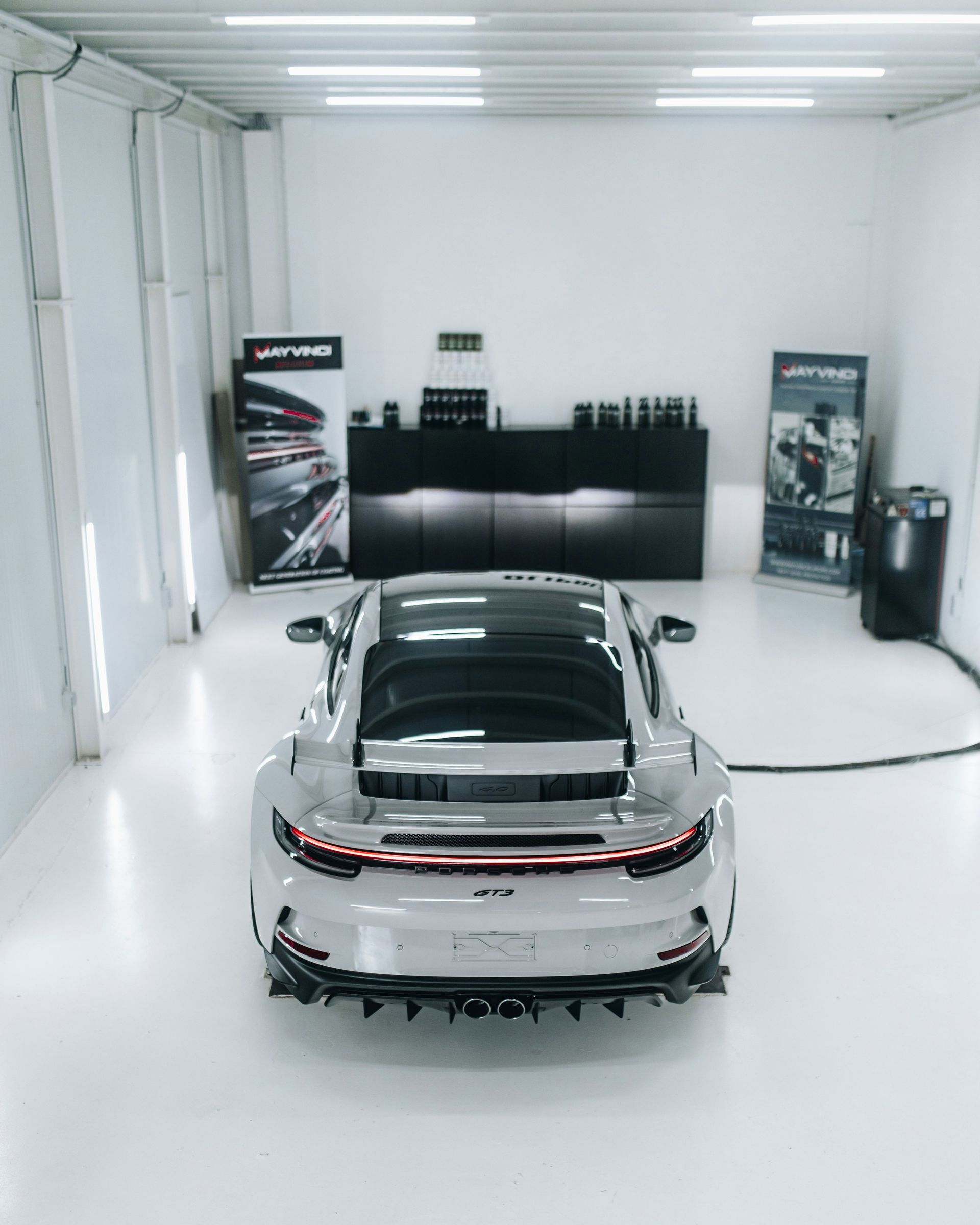 Silver sports car in a bright white garage, seen from the rear.