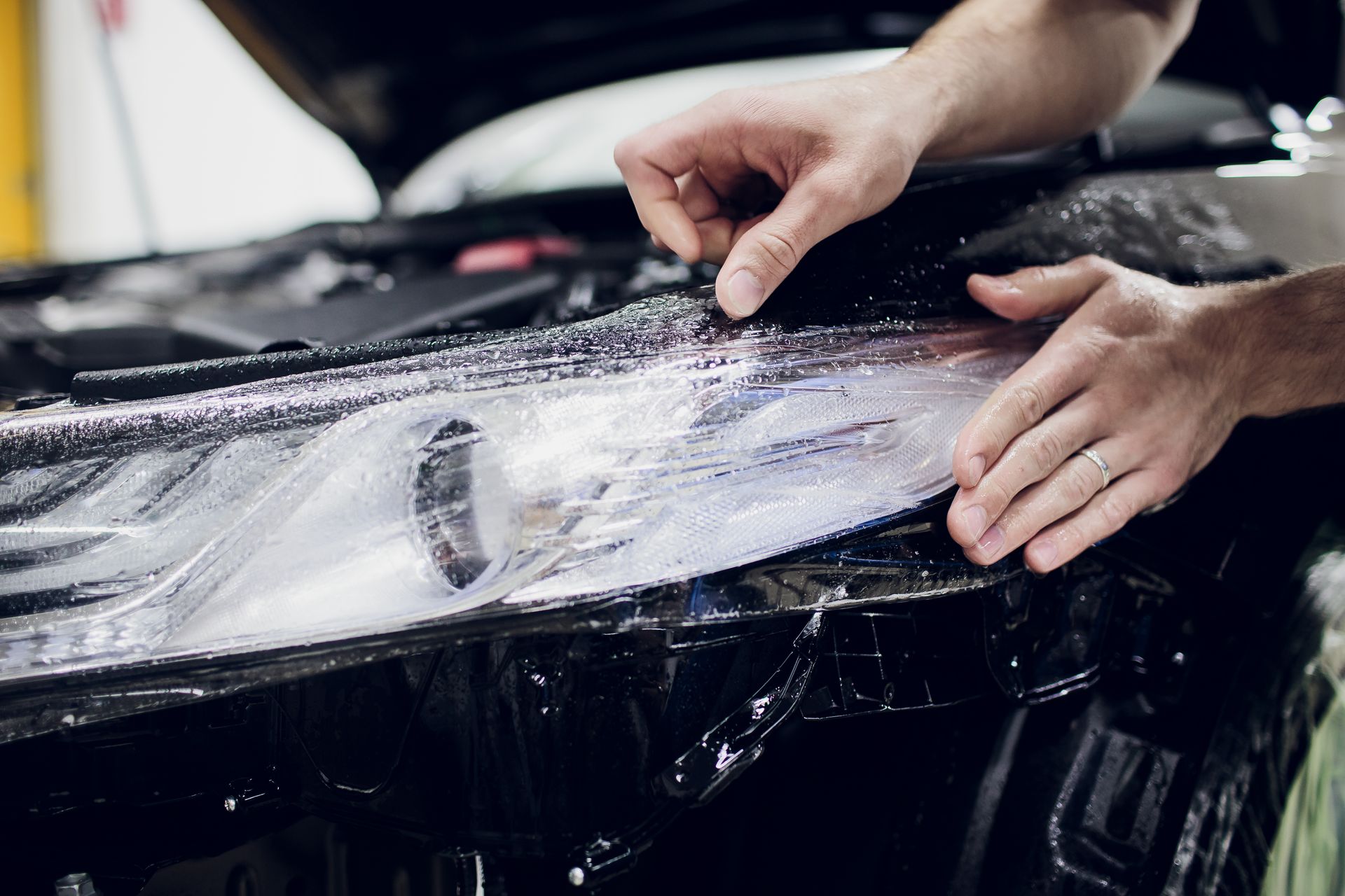 A person is installing a paint protection film on a car headlight.