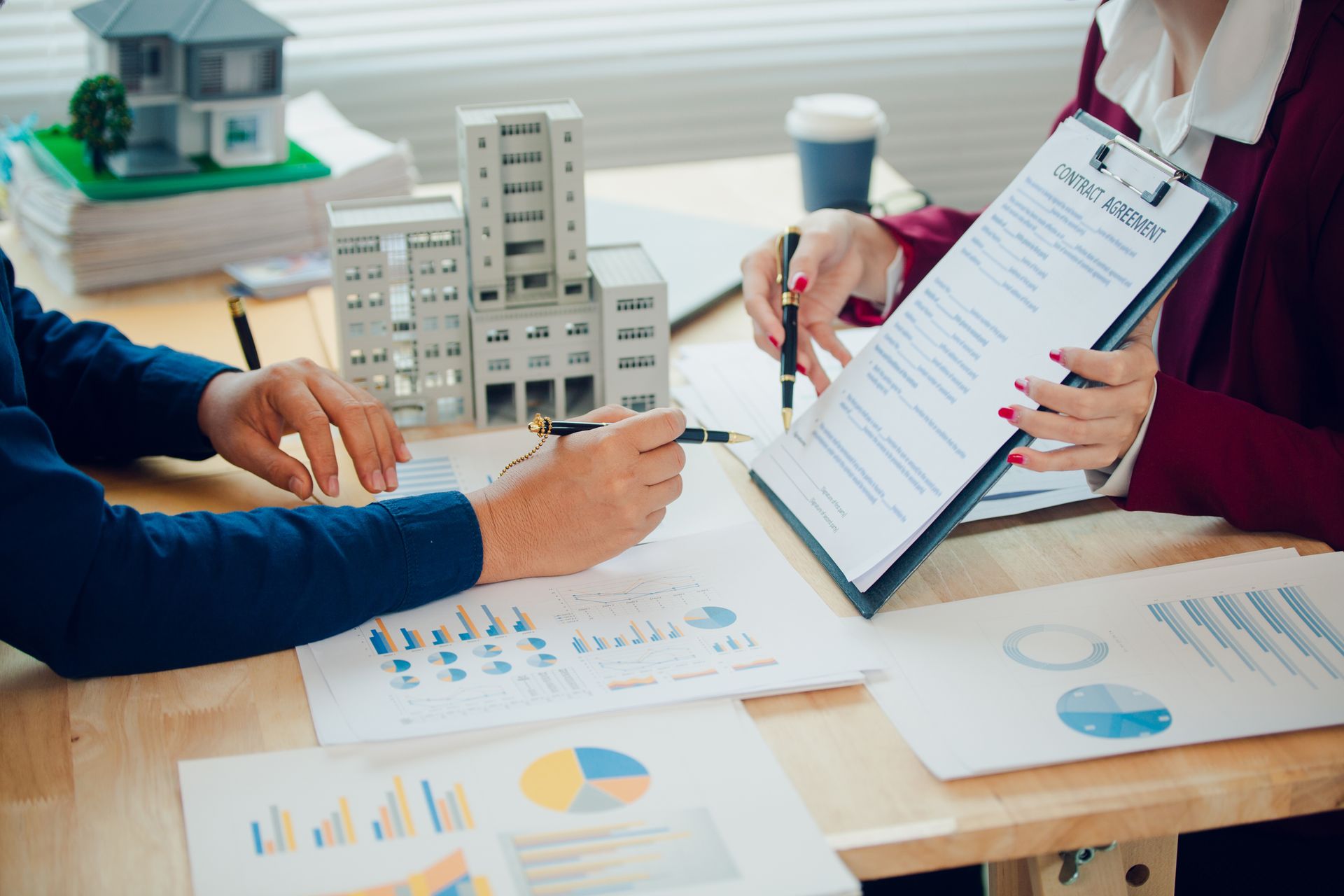 Business meeting with charts and a clipboard beside a small model building on a conference table